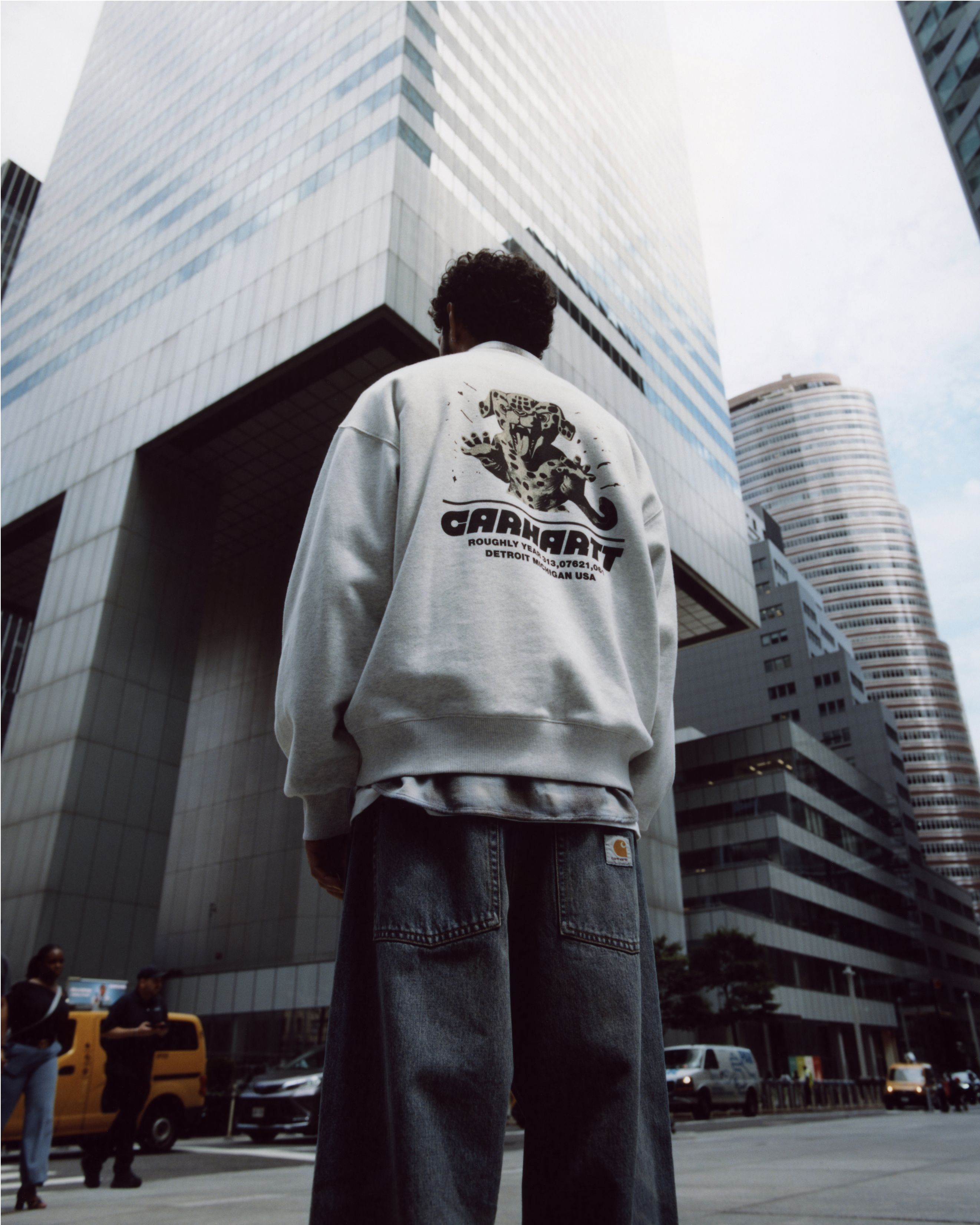 Back shot of Model standing in front of city building wearing items from the Carhartt WIP Wiptopia Collection