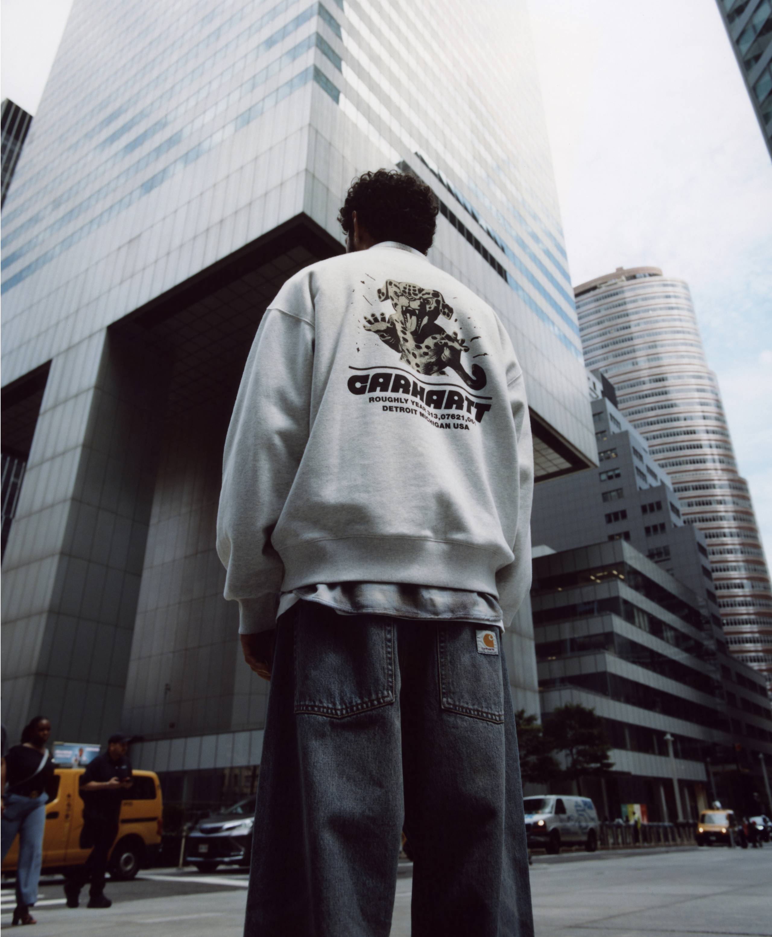Back shot of Model standing in front of city building wearing items from the Carhartt WIP Wiptopia Collection
