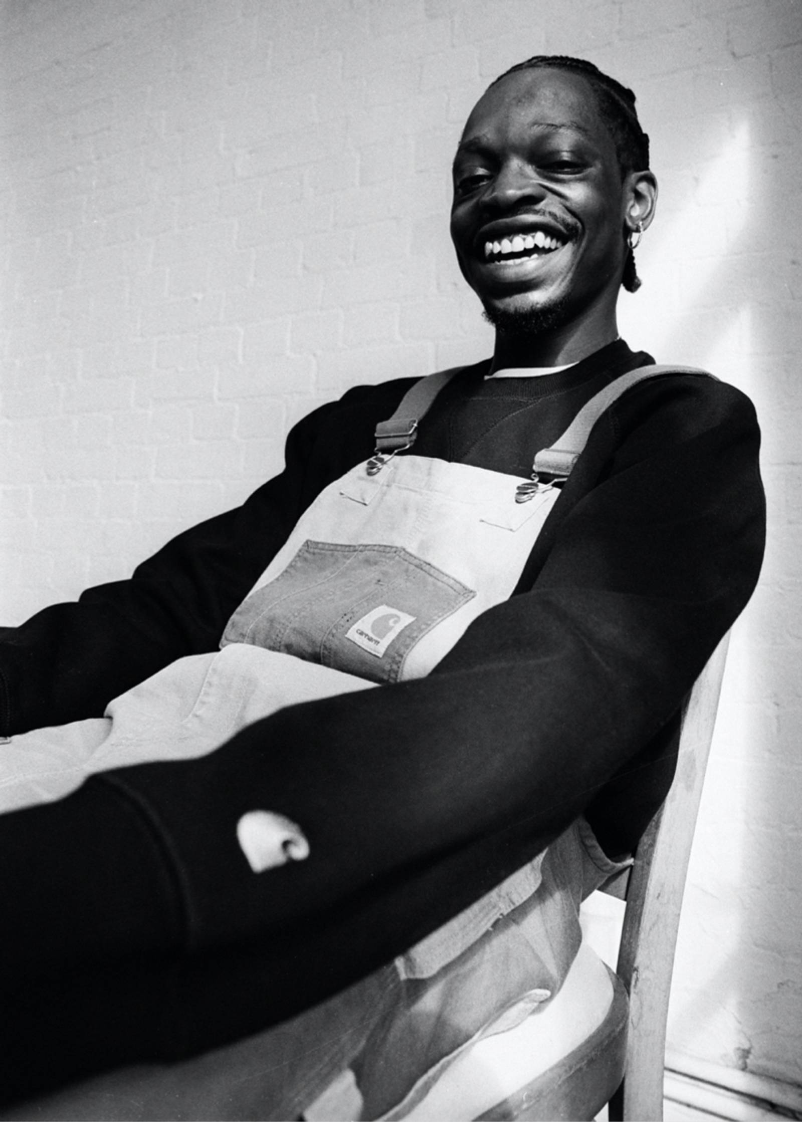 Black and white photo of seated Model wearing Carhartt WIP Double Knee Bib Overall in Two Tone Dusty Hamilton Brown