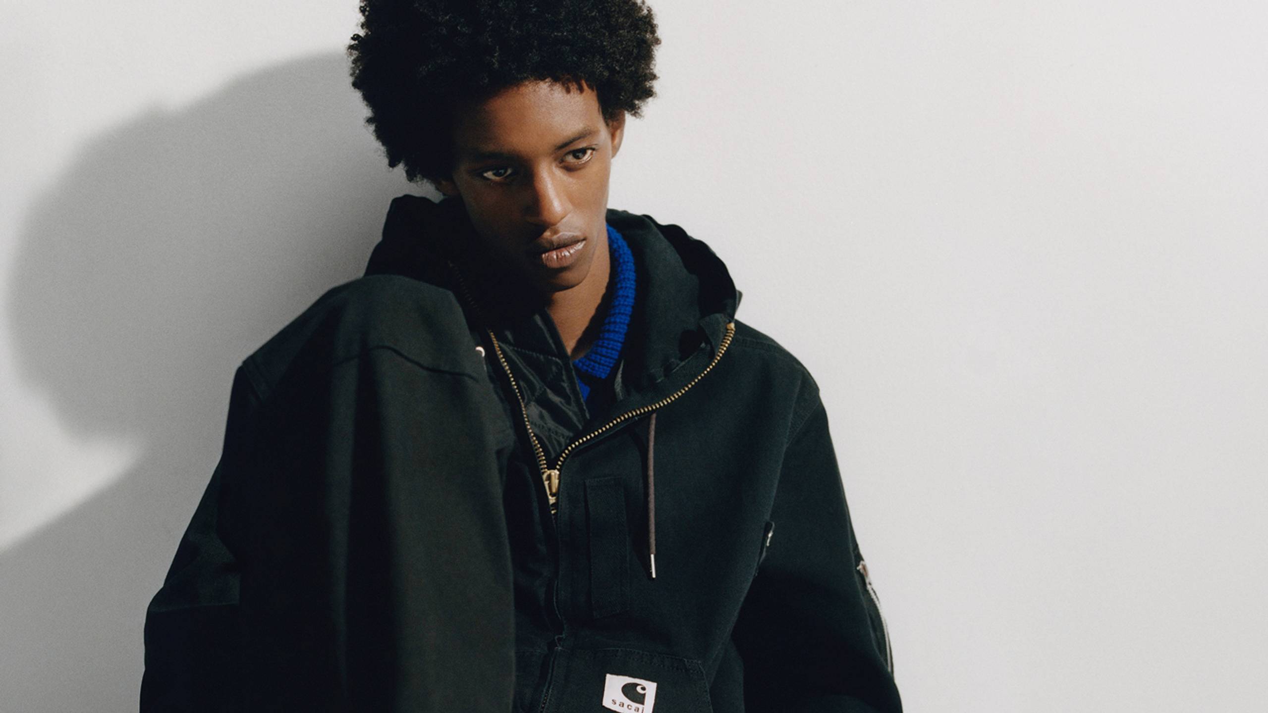 Person wearing a black sacai x Carhartt WIP hooded jacket
