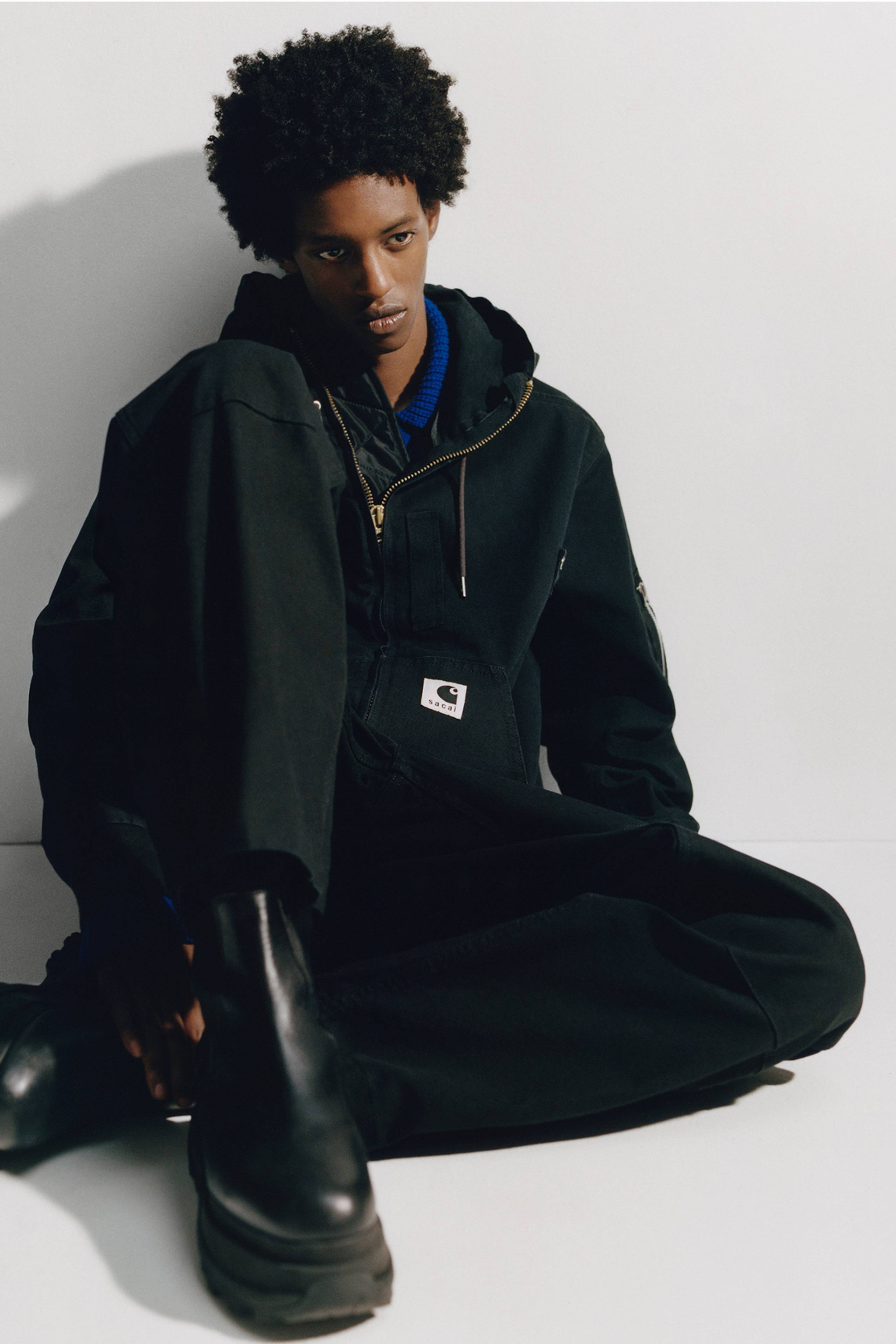 Person wearing a black sacai x Carhartt WIP hooded jacket