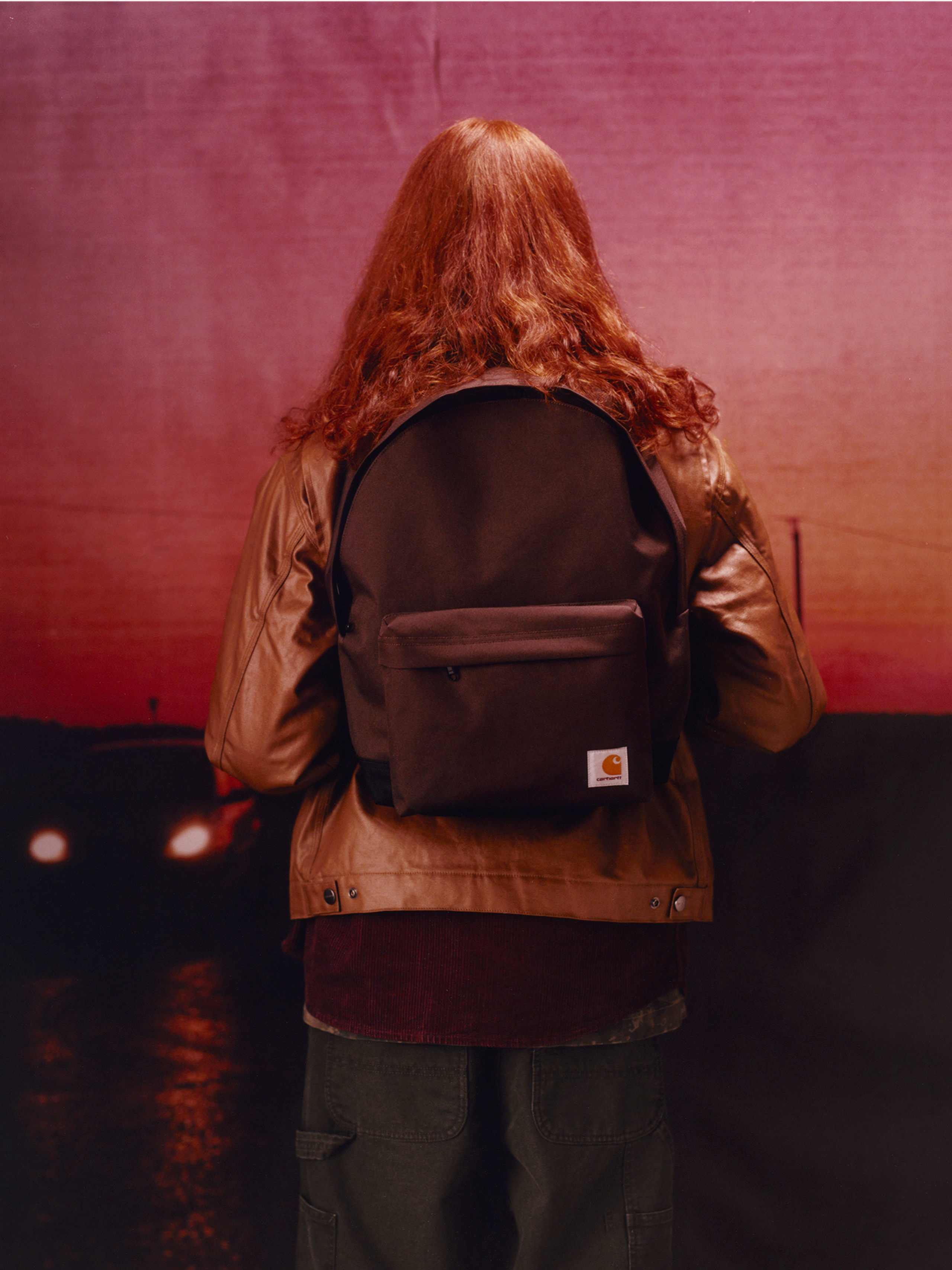 Model wearing a wax coated jacket and a brown backpack in the Carhartt WIP F/W25 Men's Lookbook