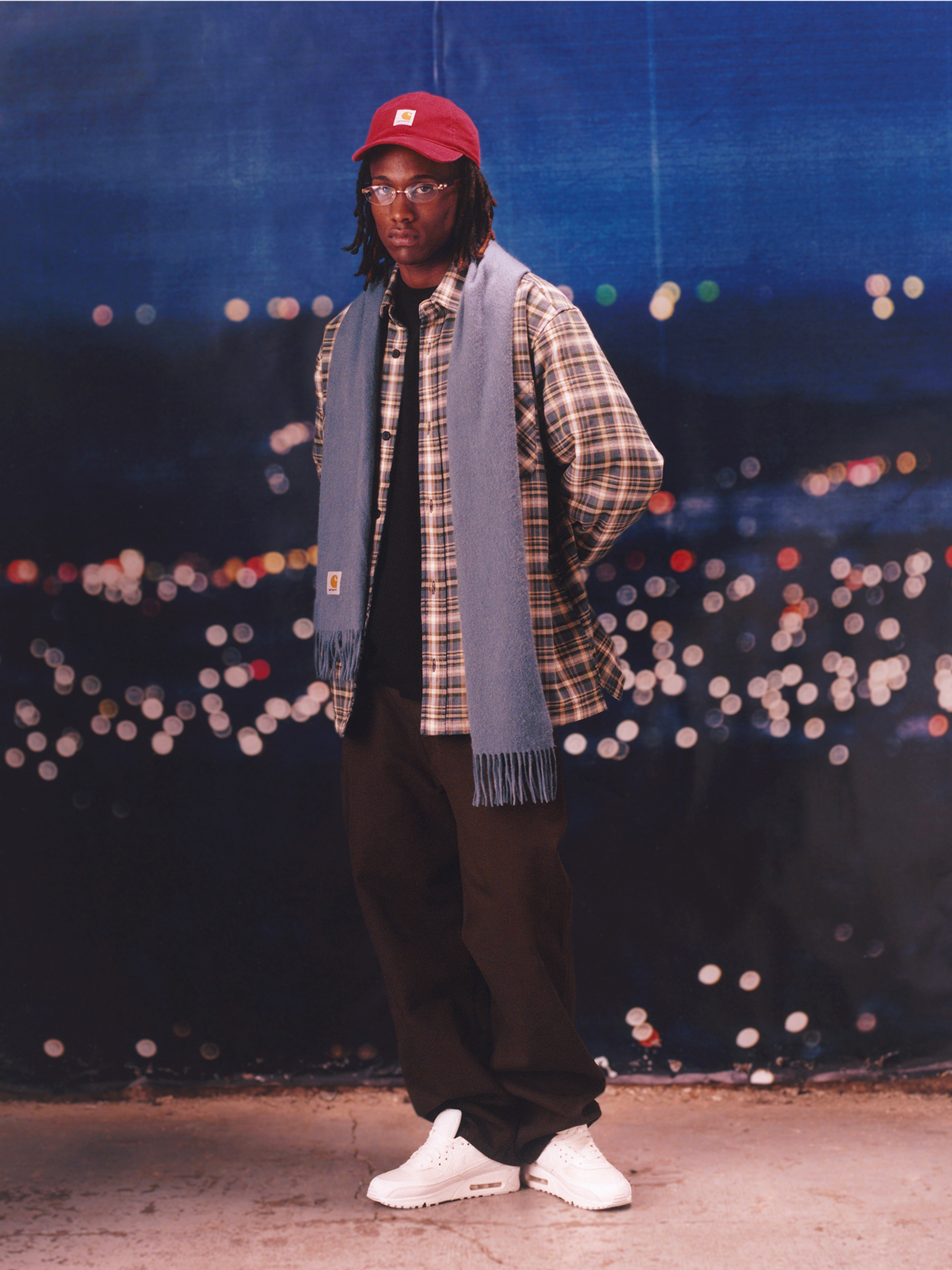 Model wearing a red hat, flannel shirt and blue scarf in the Carhartt WIP F/W25 Men's Lookbook