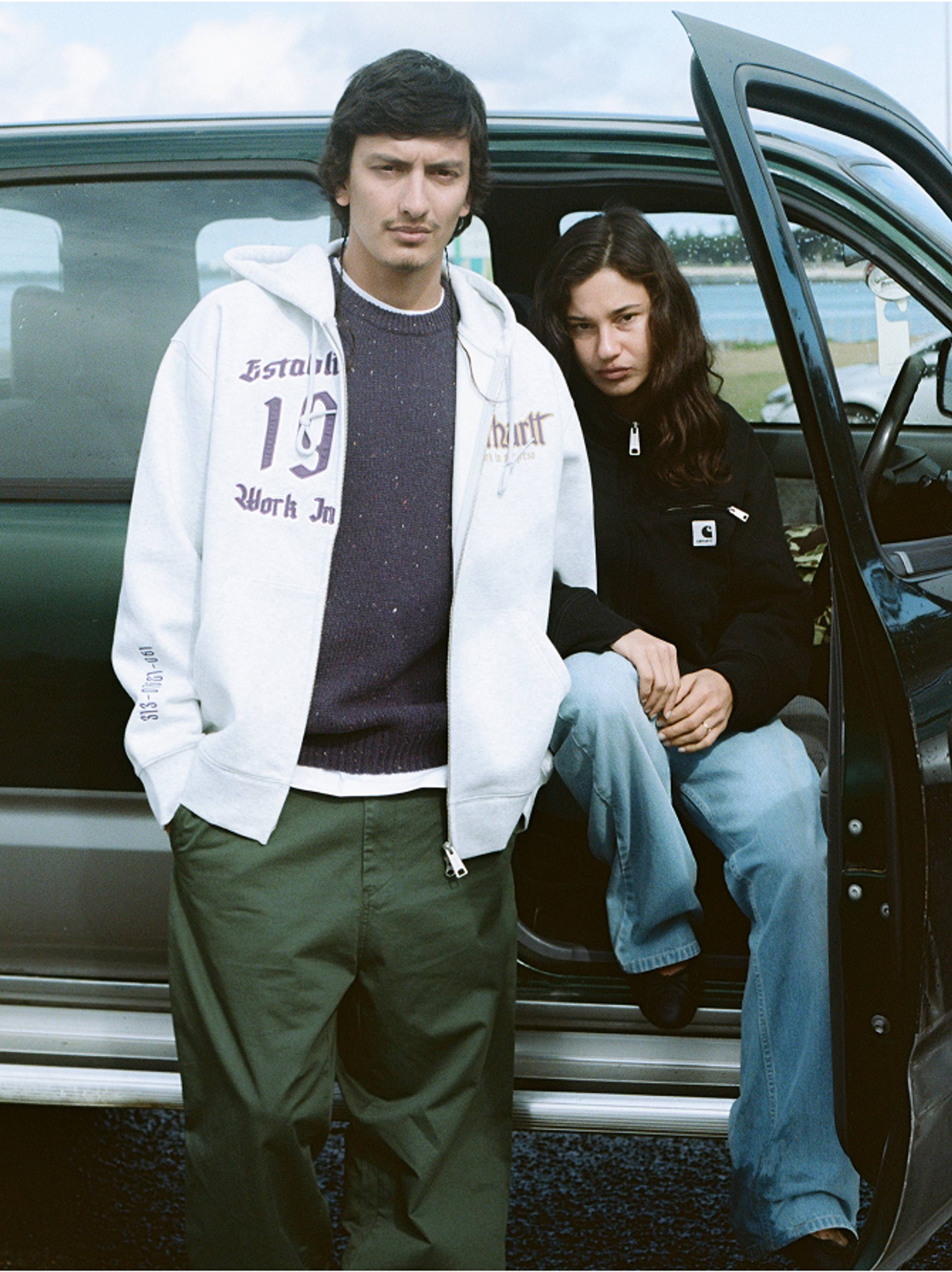 Person on the left wearin green pants and zip up sweatshirt, person on the right wearing a black detroit jacket
