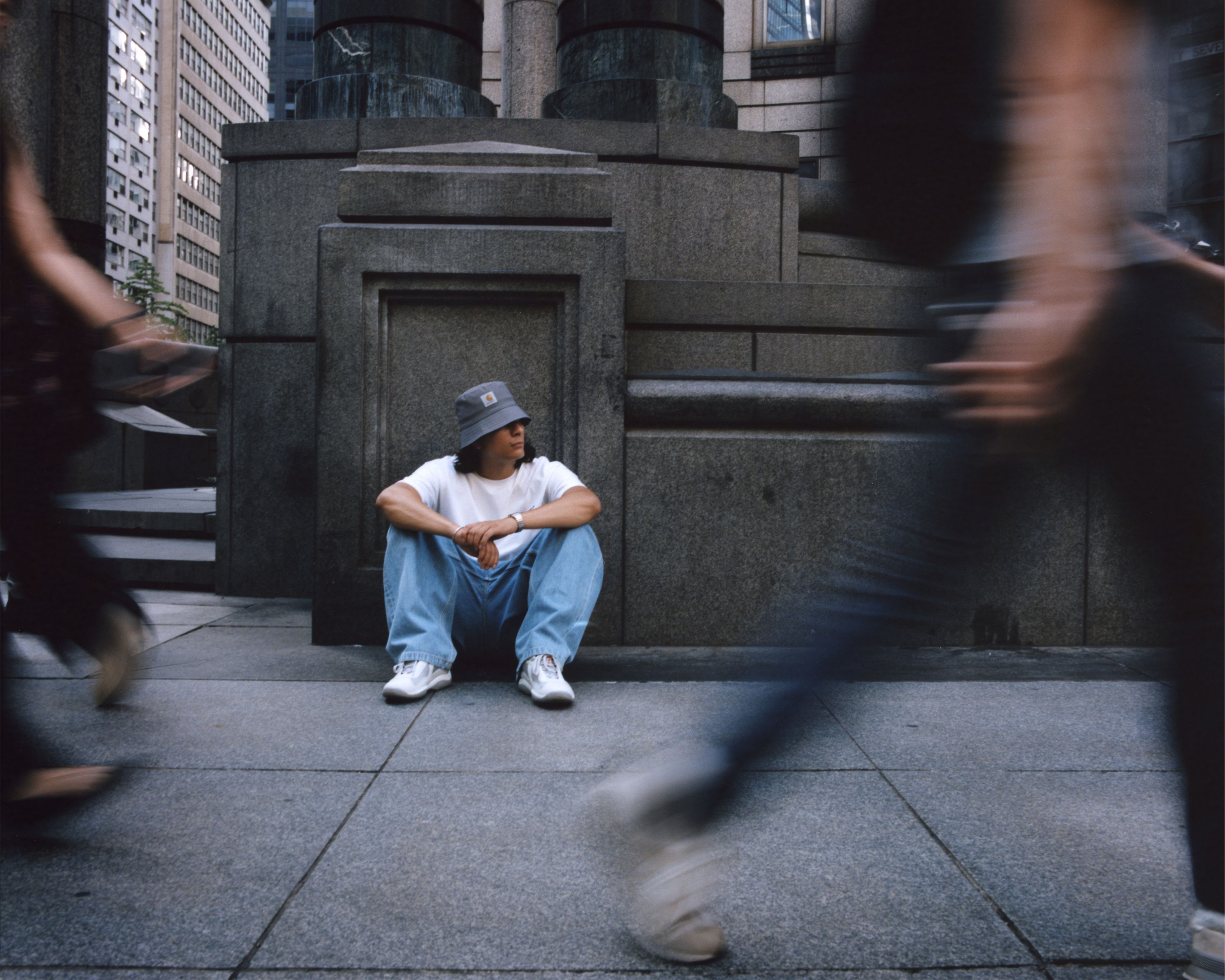 Model sitting in front of city building wearing items from the Carhartt WIP Wiptopia Collection