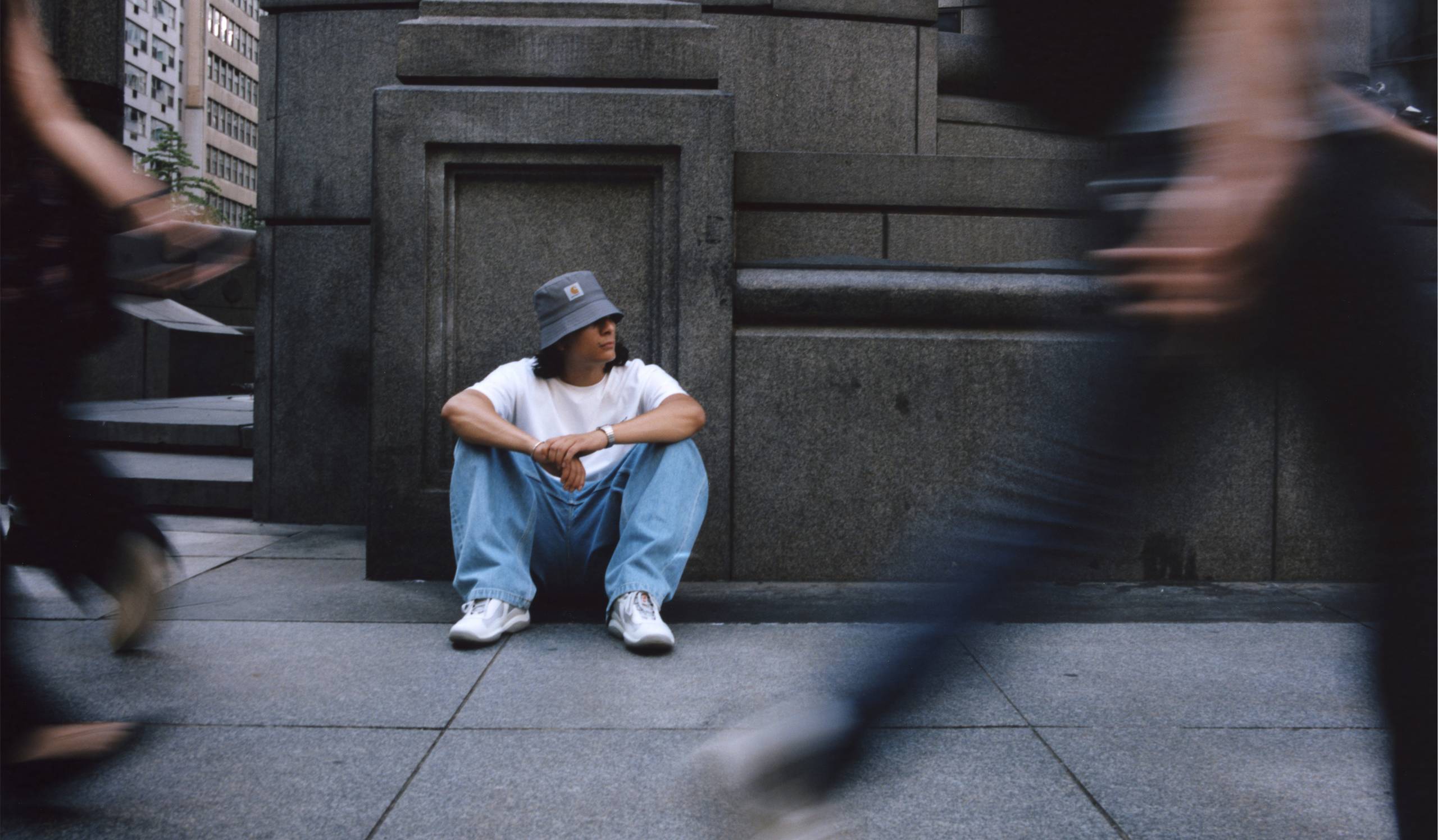 Model sitting in front of city building wearing items from the Carhartt WIP Wiptopia Collection