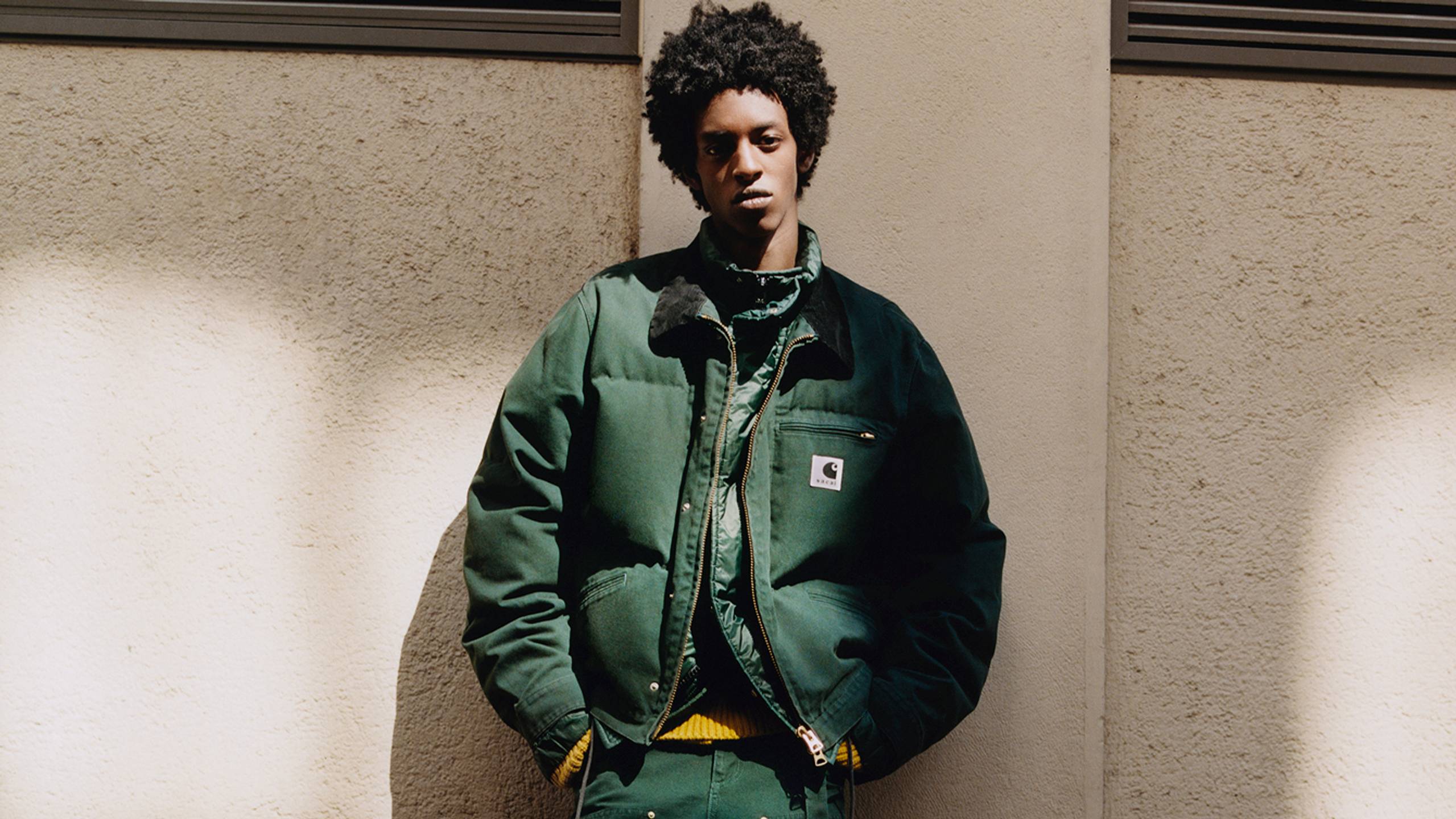Person wearing a green sacai x Carhartt WIP zip up puffer jacket and green double knee pants