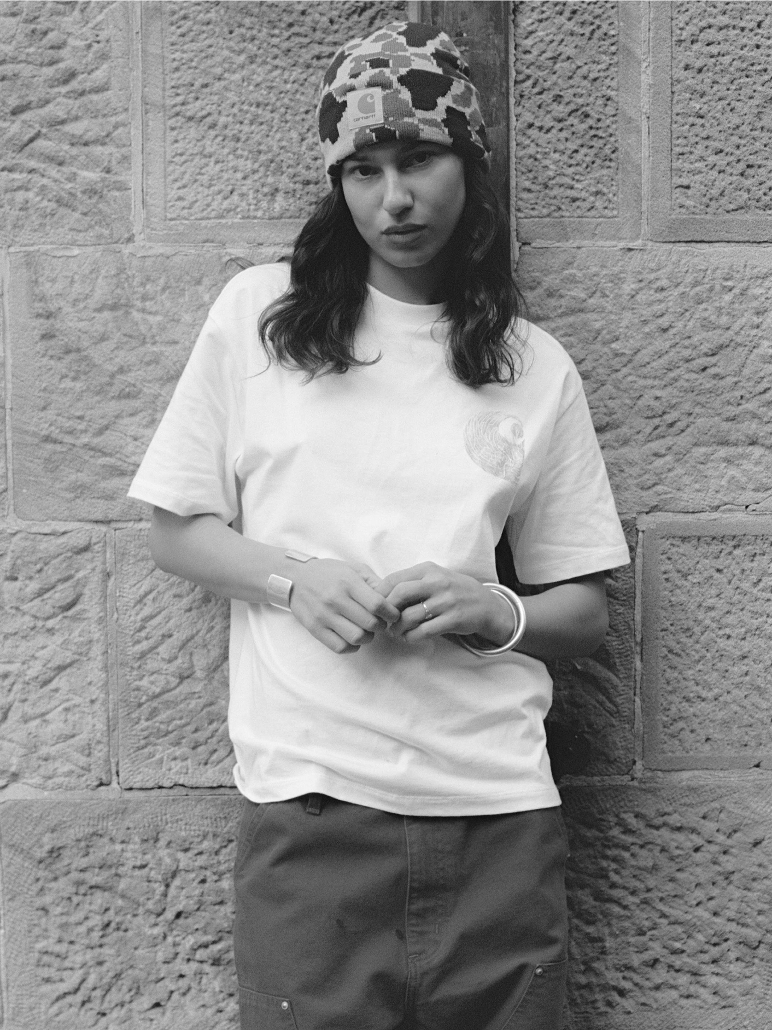 A black and white photo of a person in a white t-shirt and camo Prentis beanie