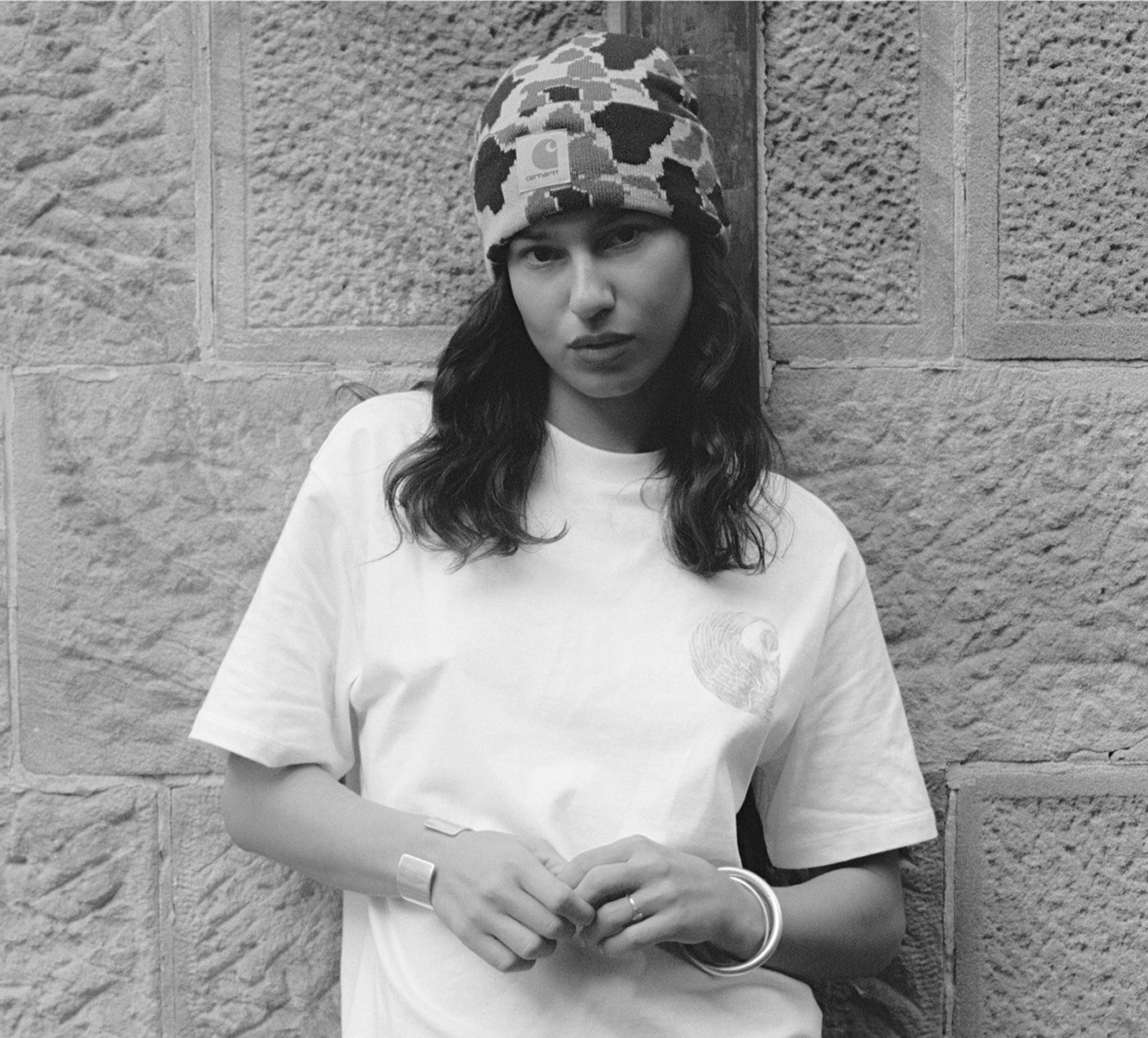 A black and white photo of a person in a white t-shirt and camo Prentis beanie
