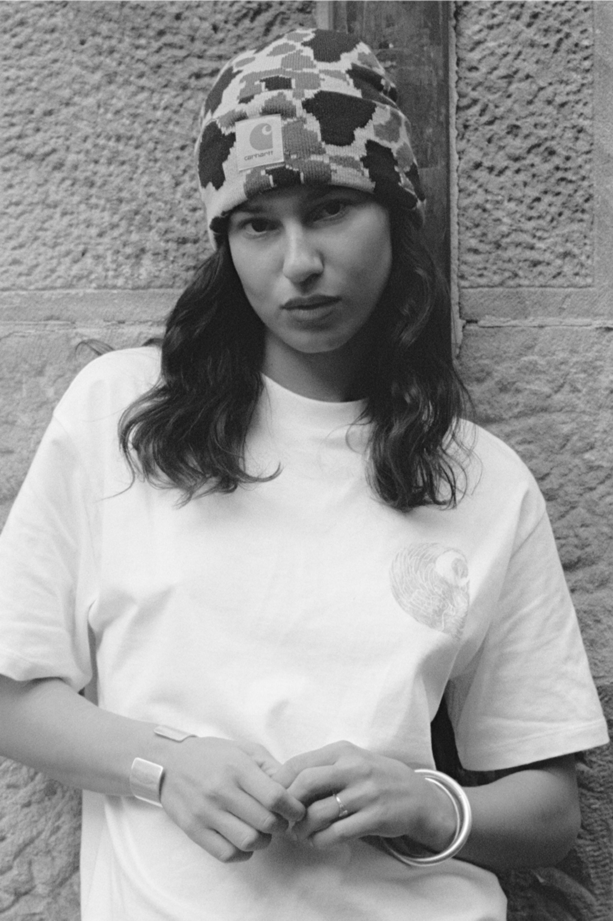 A black and white photo of a person in a white t-shirt and camo Prentis beanie