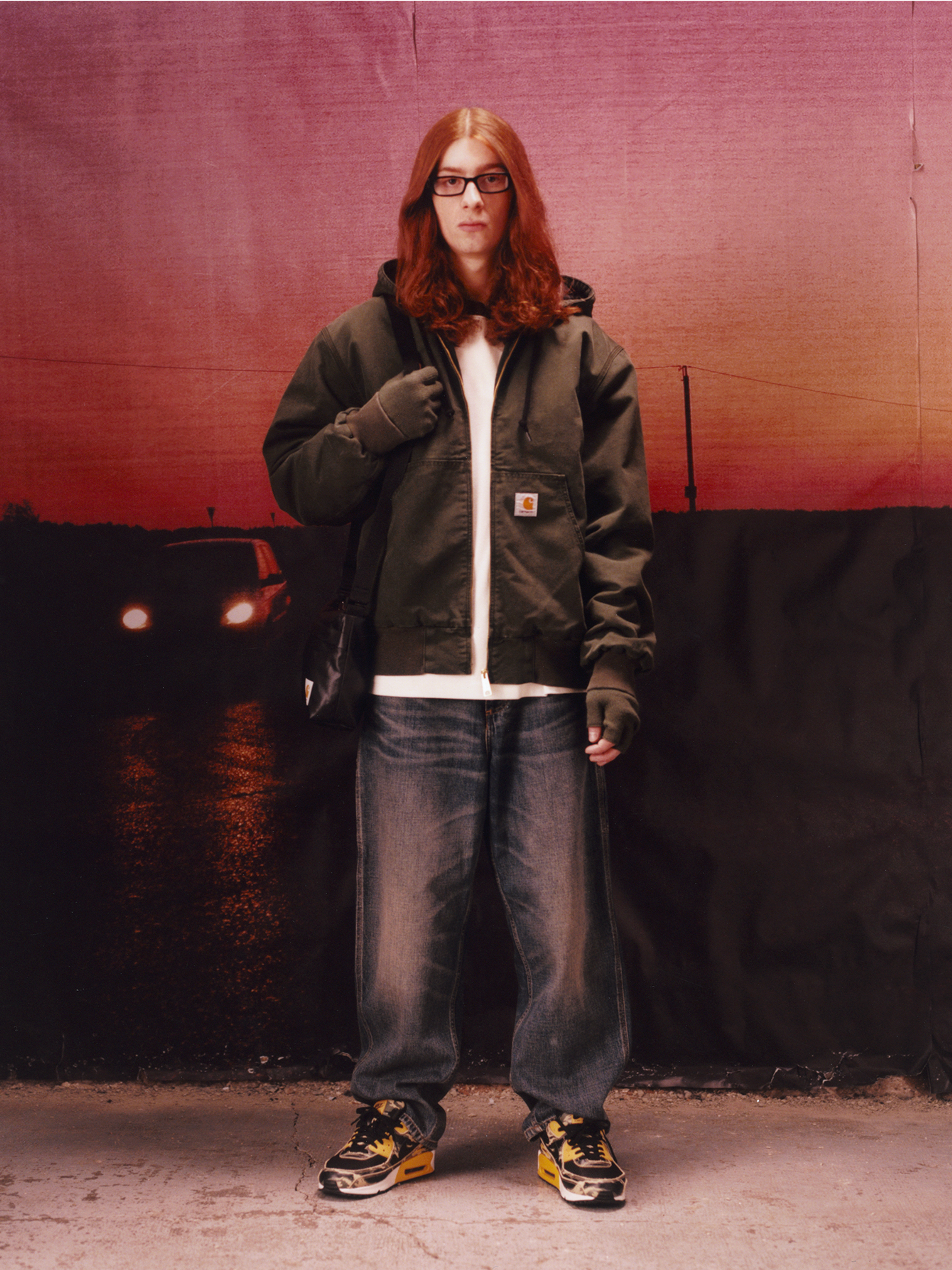 Model wearing a green active jacket and blue light washed pants in the Carhartt WIP F/W25 Men's Lookbook