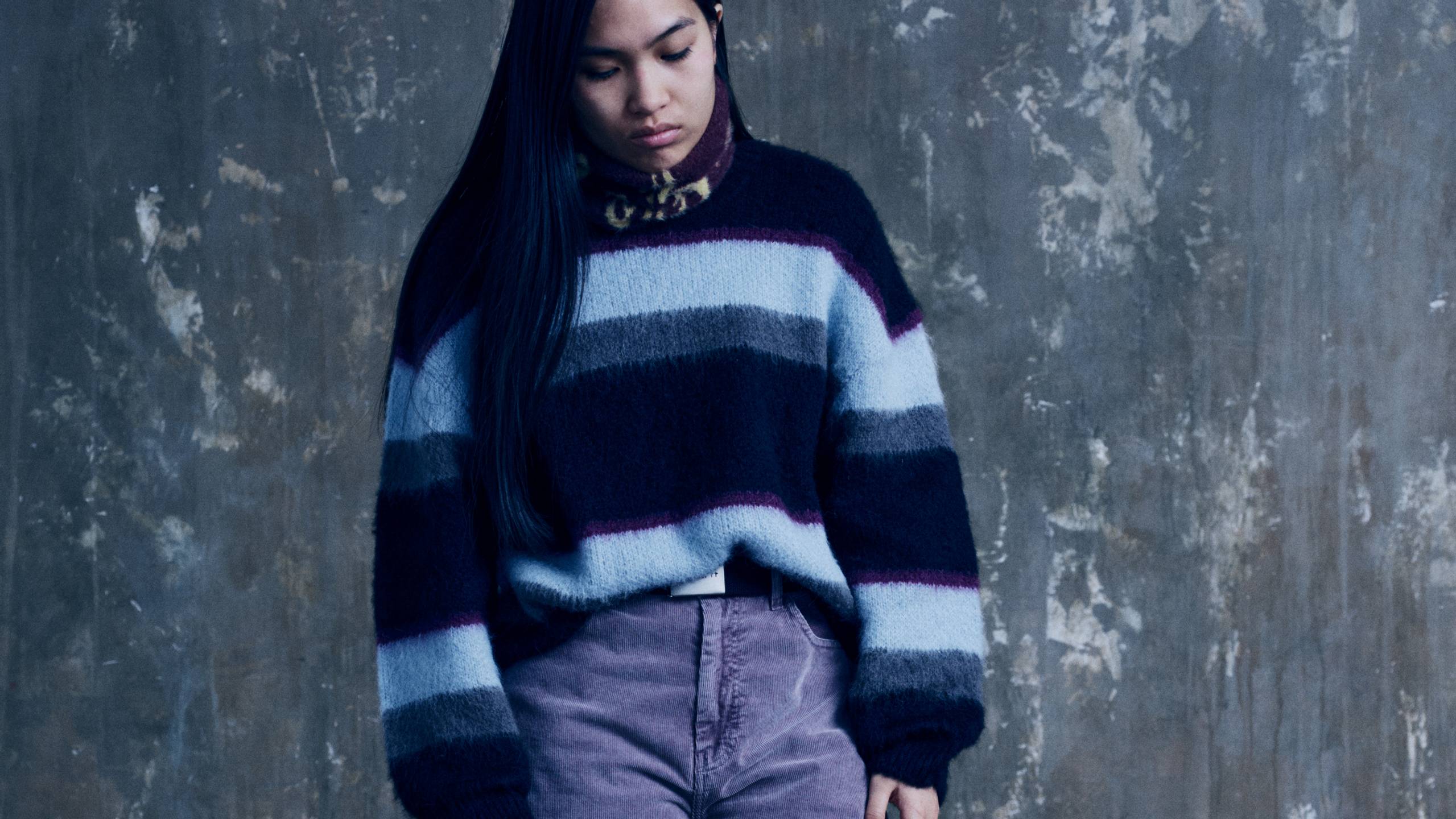Model wearing a Women’s Merlin Sweater in Citadel and a pair of purple pants