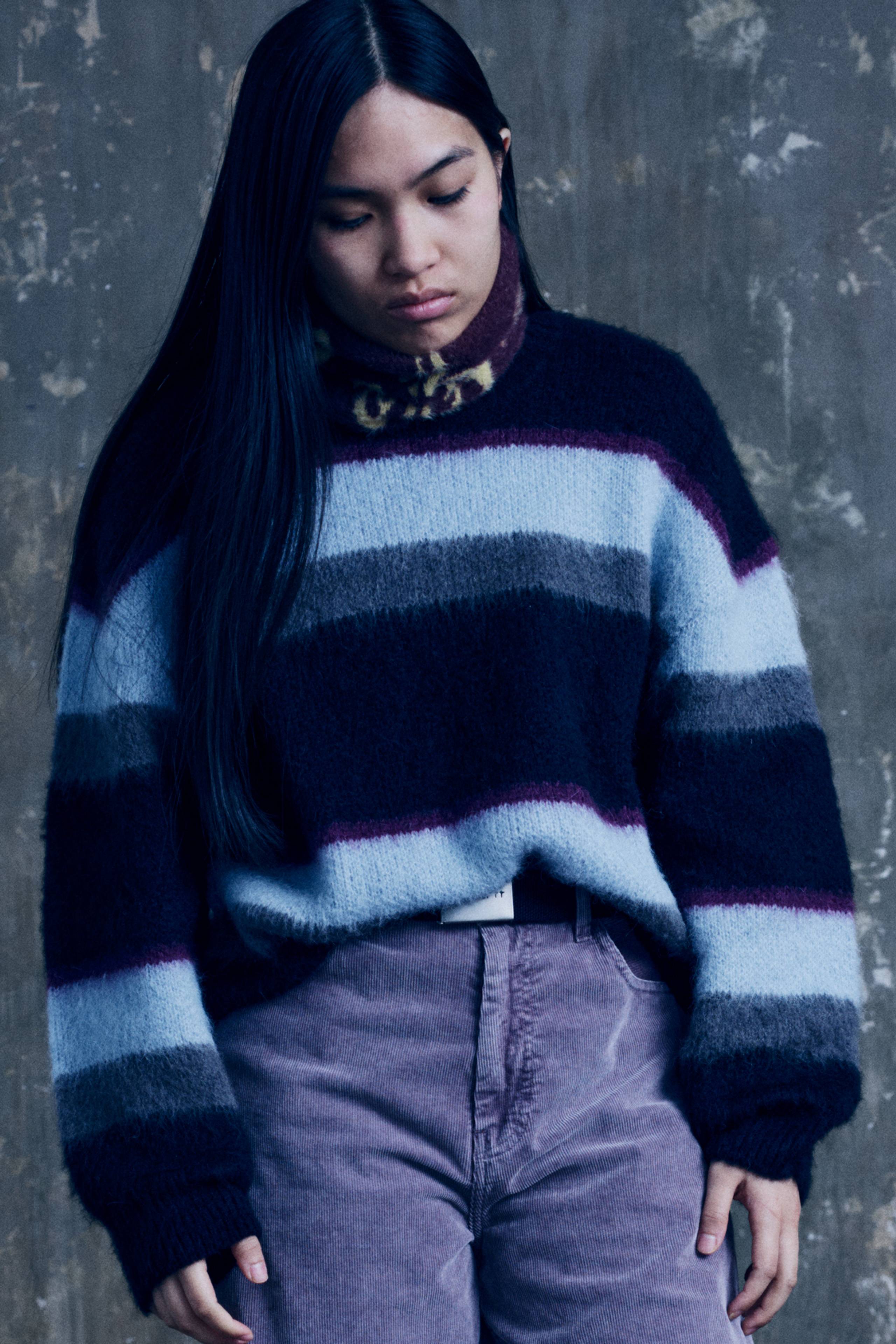 Model wearing a Women’s Merlin Sweater in Citadel and a pair of purple pants
