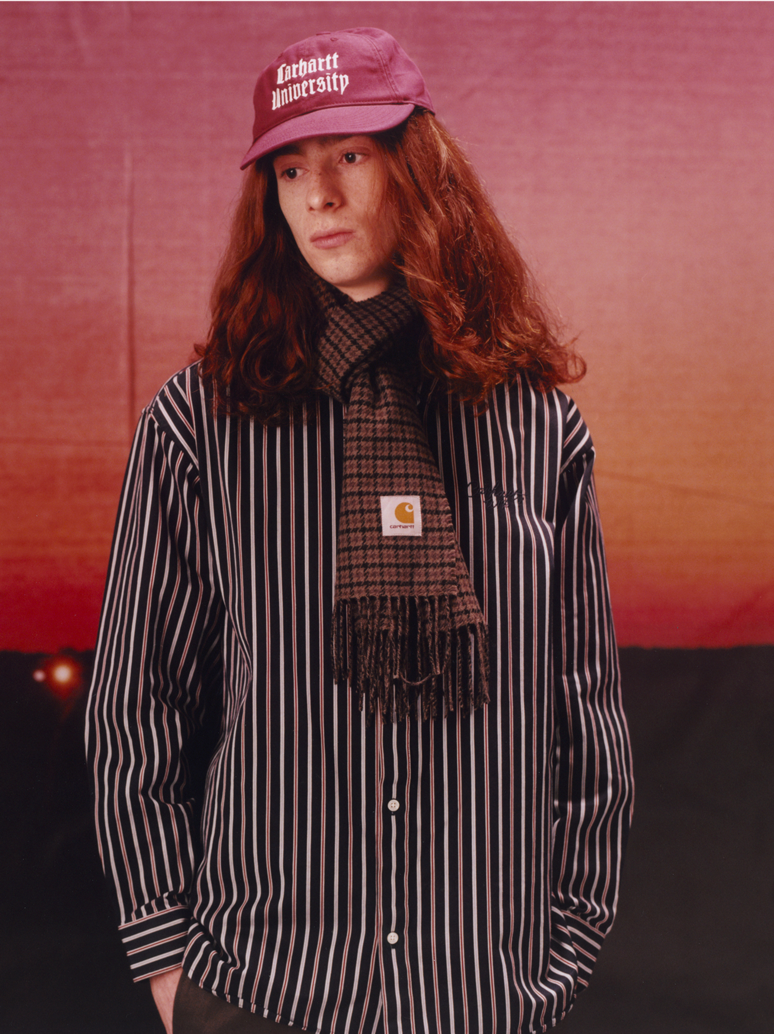 Model wearing a red hat, stripe shirt and plaid scarf in the Carhartt WIP F/W25 Men's Lookbook
