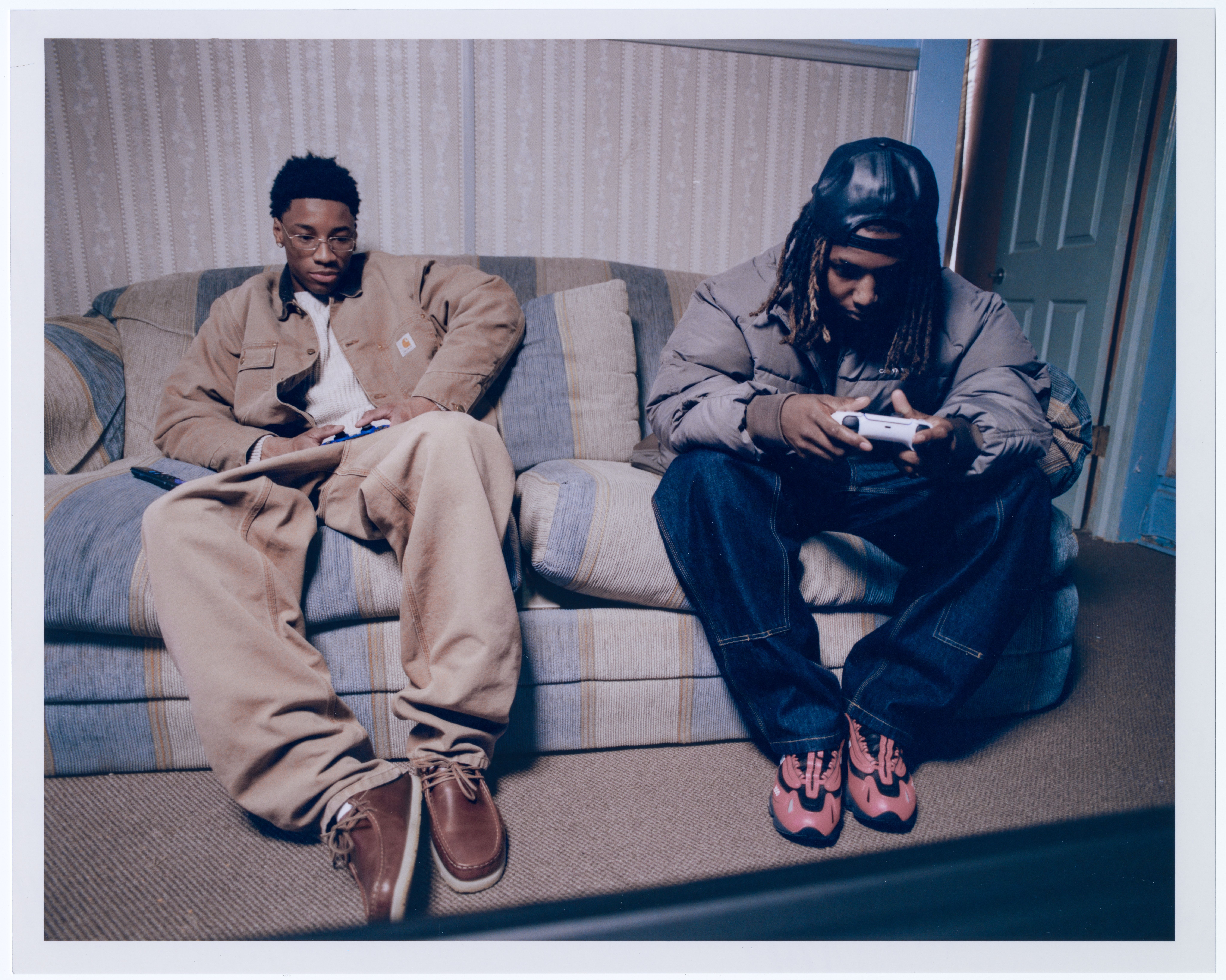 Models sitting on a couch wearing Carhartt WIP items in the Fall 2025 Campaign shot by Dan Regan
