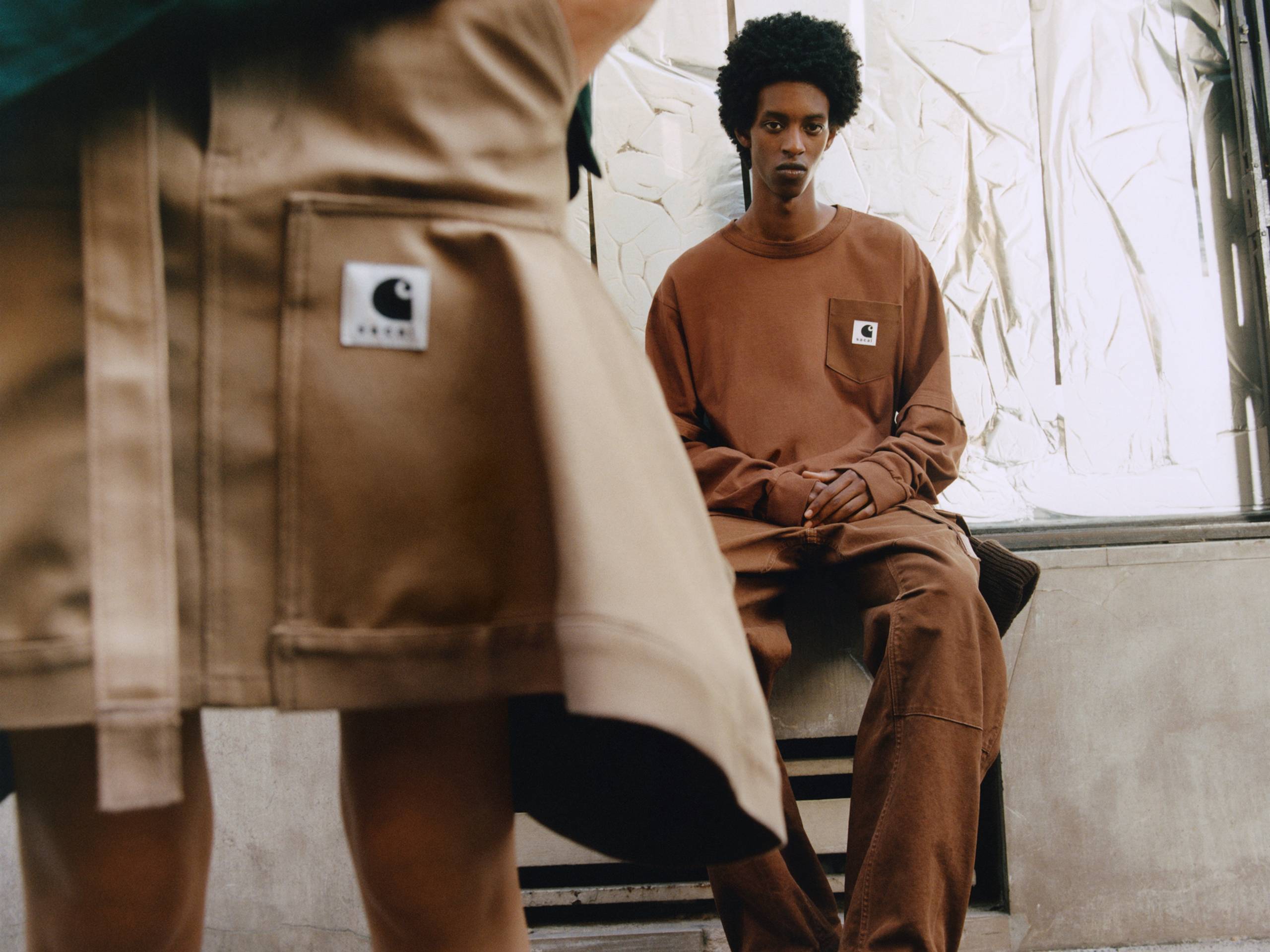 Person wearing a brown sacai x Carhartt WIP long sleeve t-shirt with a sacai x Carhartt WIP skirt in the foreground