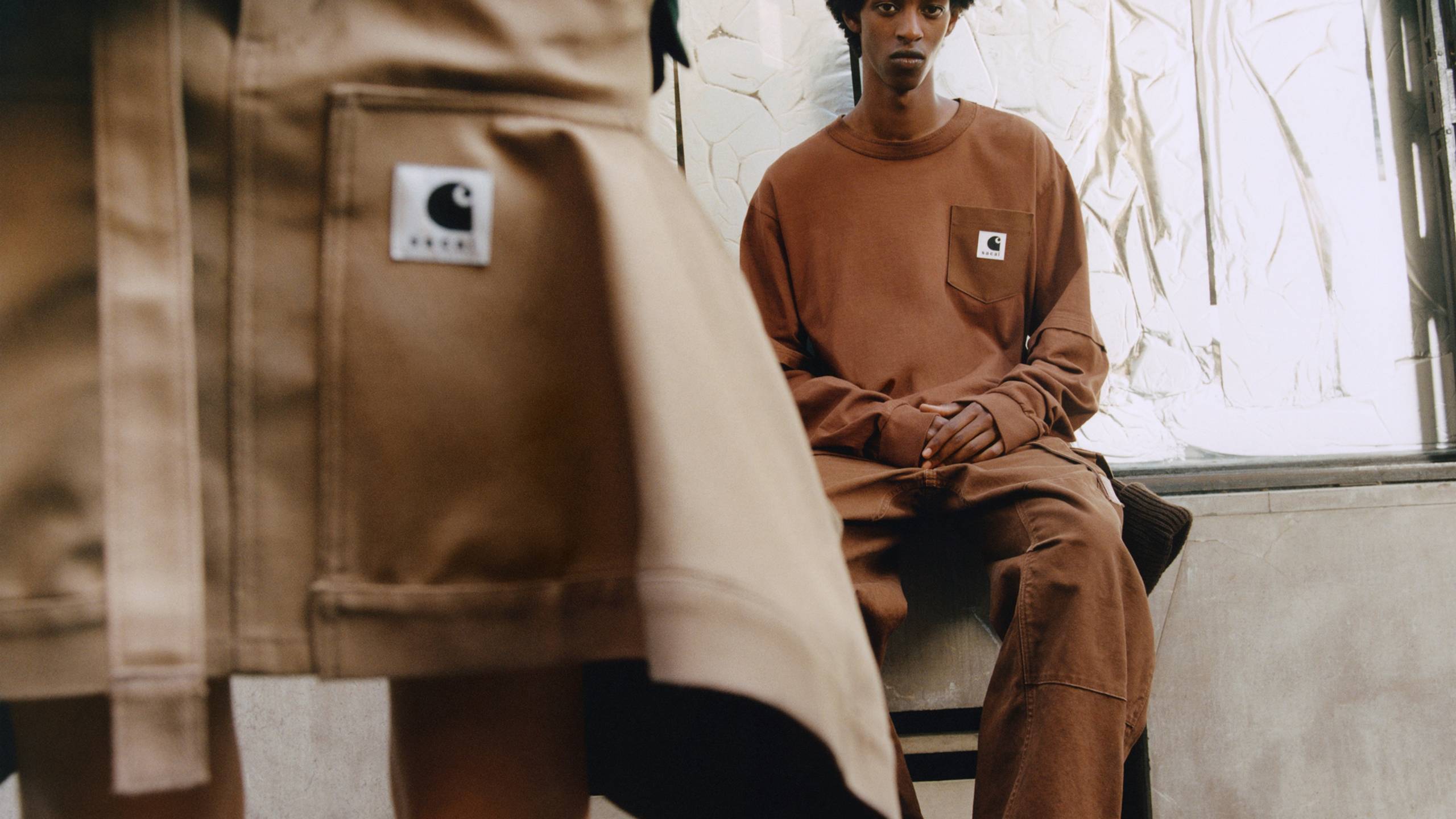 Person wearing a brown sacai x Carhartt WIP long sleeve t-shirt with a sacai x Carhartt WIP skirt in the foreground