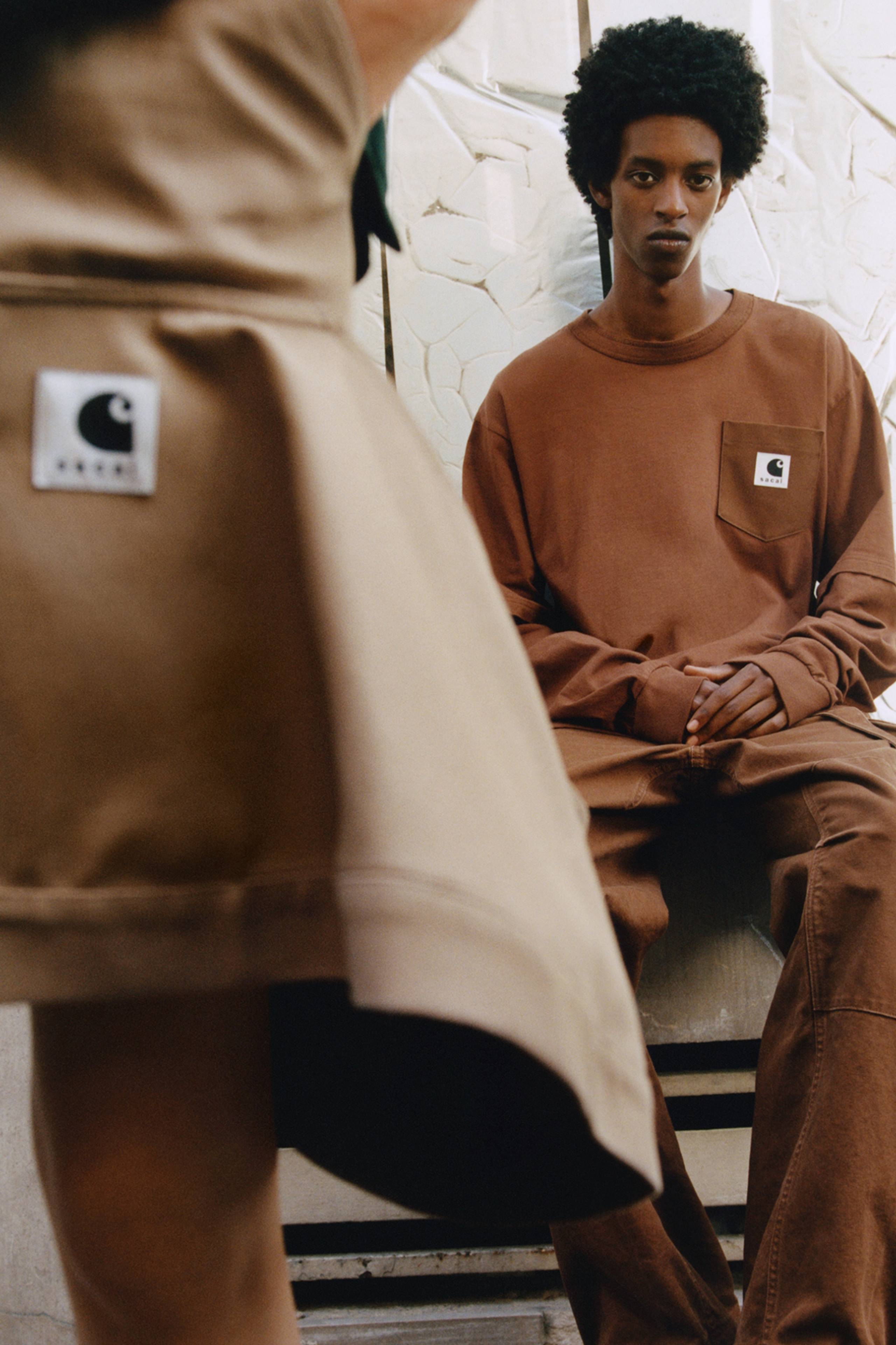 Person wearing a brown sacai x Carhartt WIP long sleeve t-shirt with a sacai x Carhartt WIP skirt in the foreground