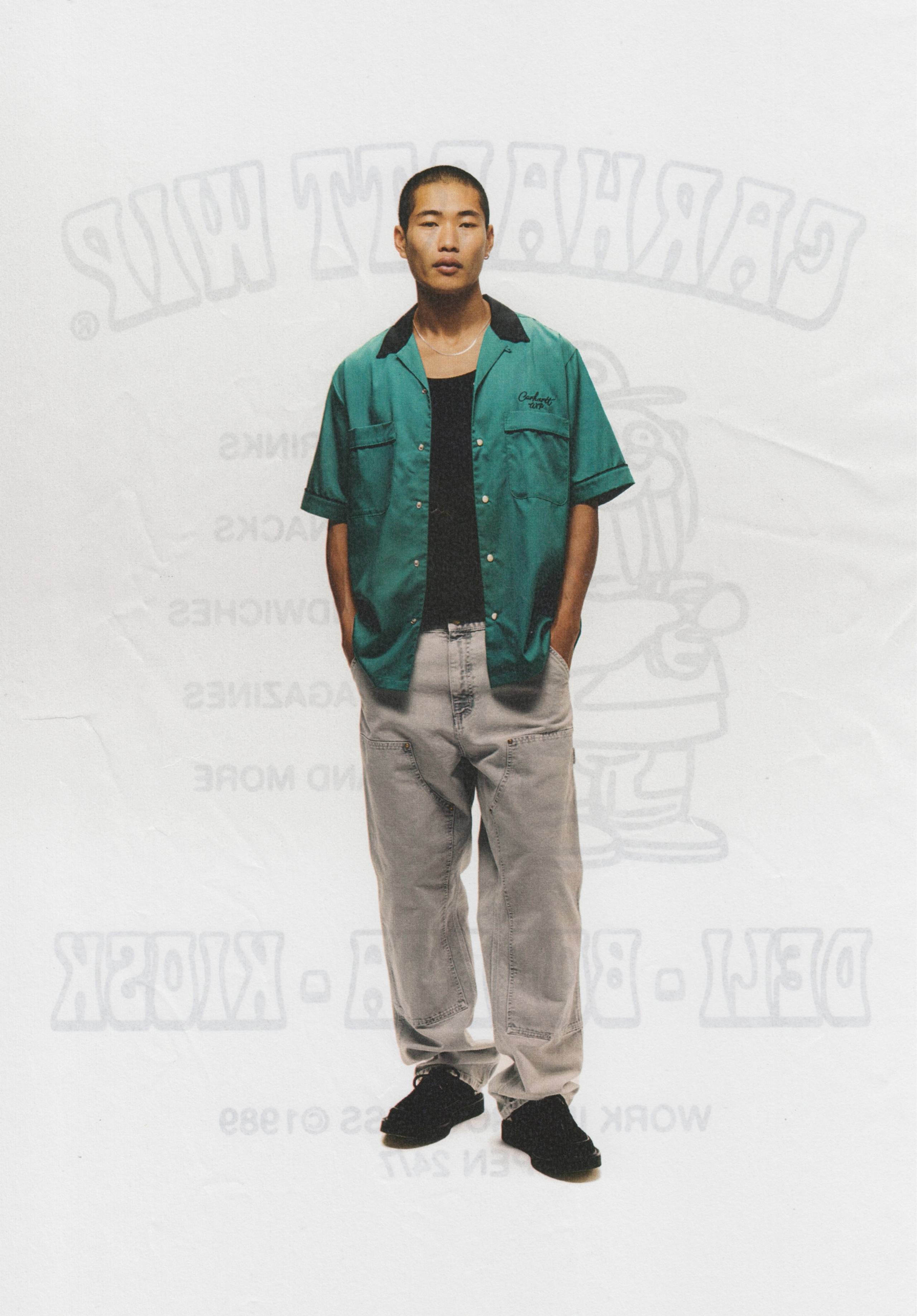 Model wearing a pair of Carhartt WIP Double Knee Pants in Chalk Wash and green Bowl Shirt