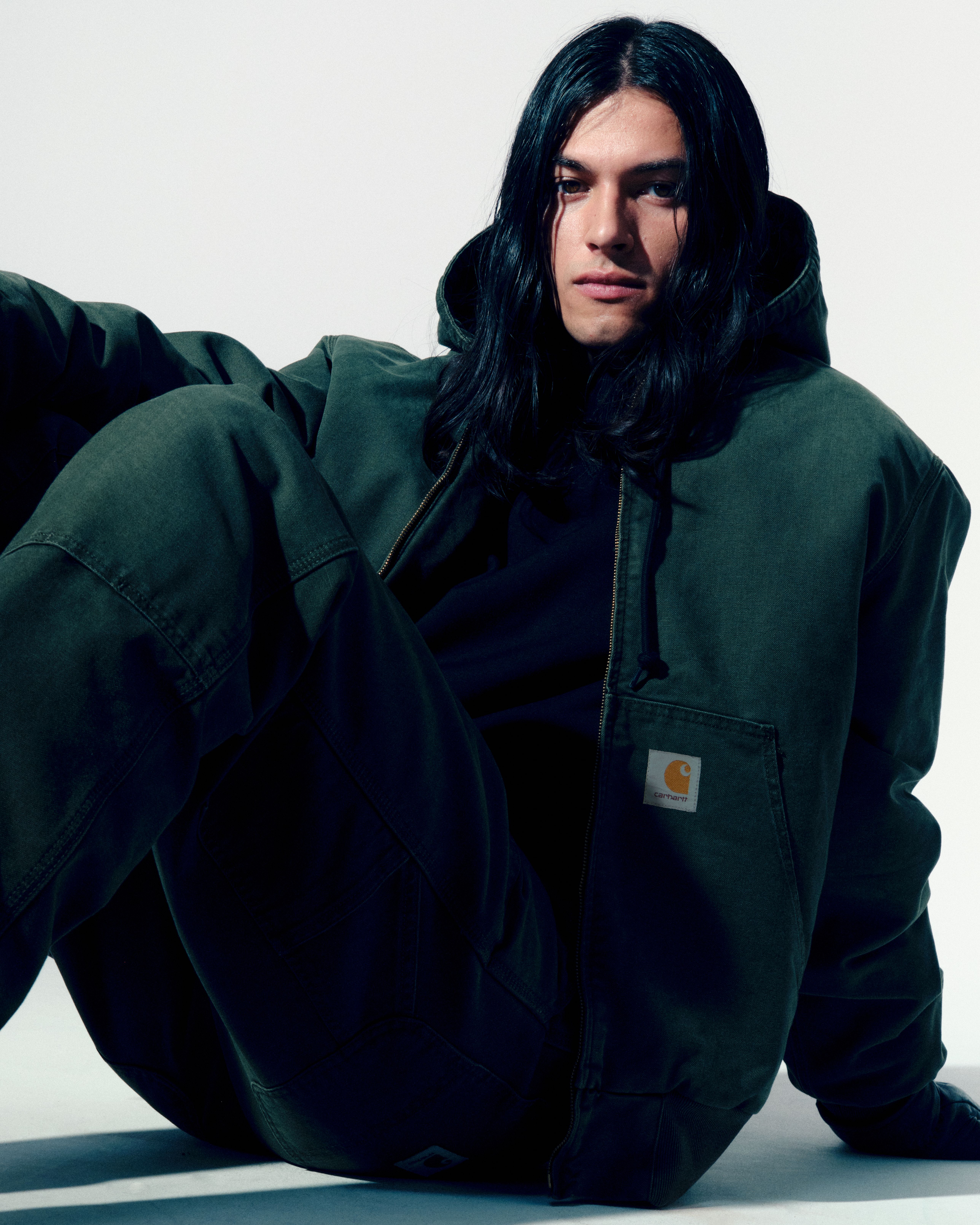Model sitting on the floor wearing an Active Jacket and Double Knee Pants in Olive