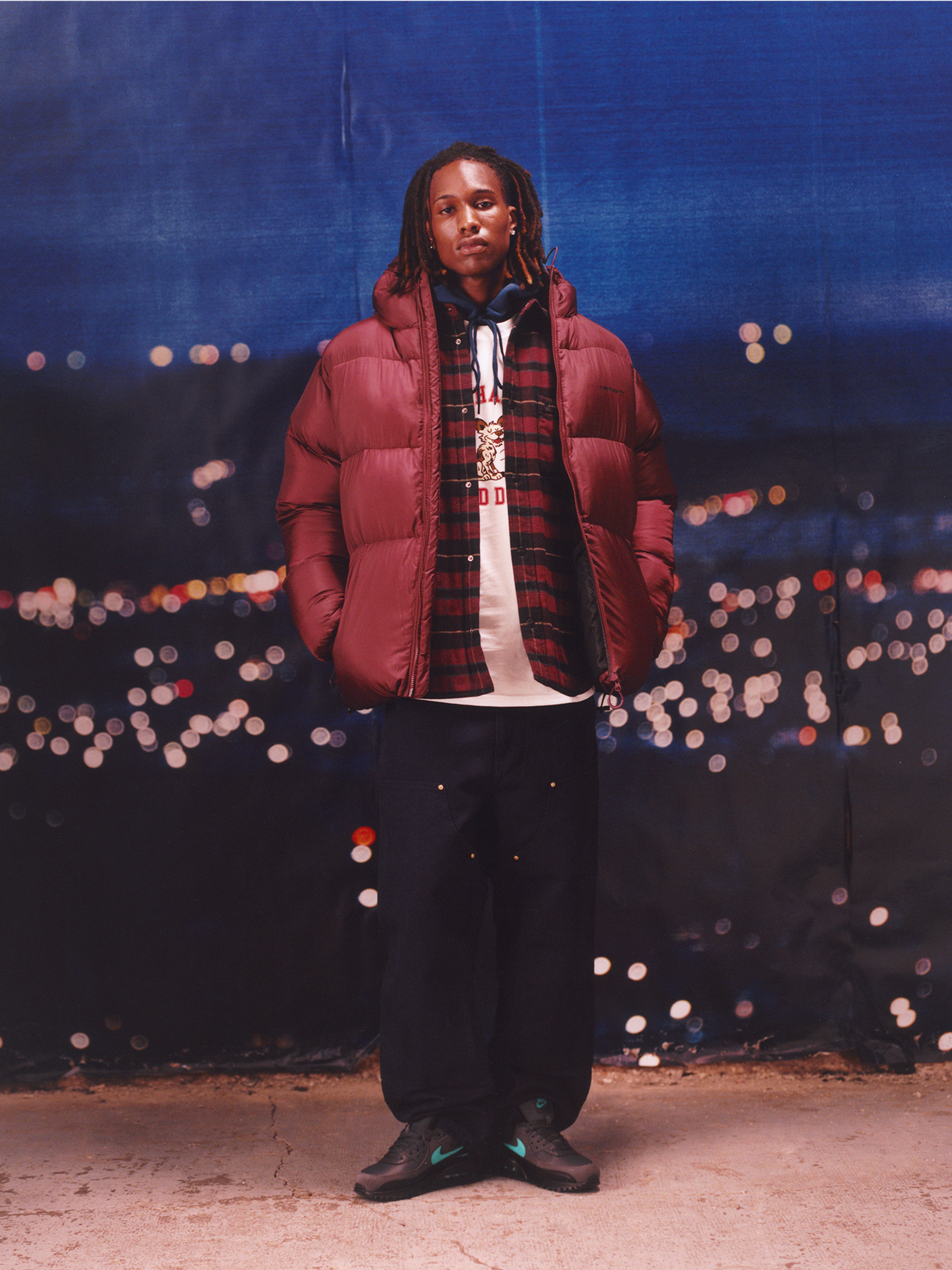 Model wearing a red puffer jacket, flannel shirt and double knee pants in the Carhartt WIP F/W25 Men's Lookbook