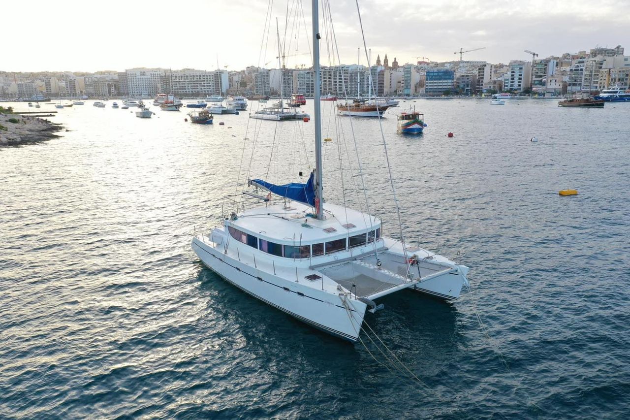 La Zingara, a Lagoon 450 sailing catamaran, anchored in clear Maltese water with trampoline nets forward.