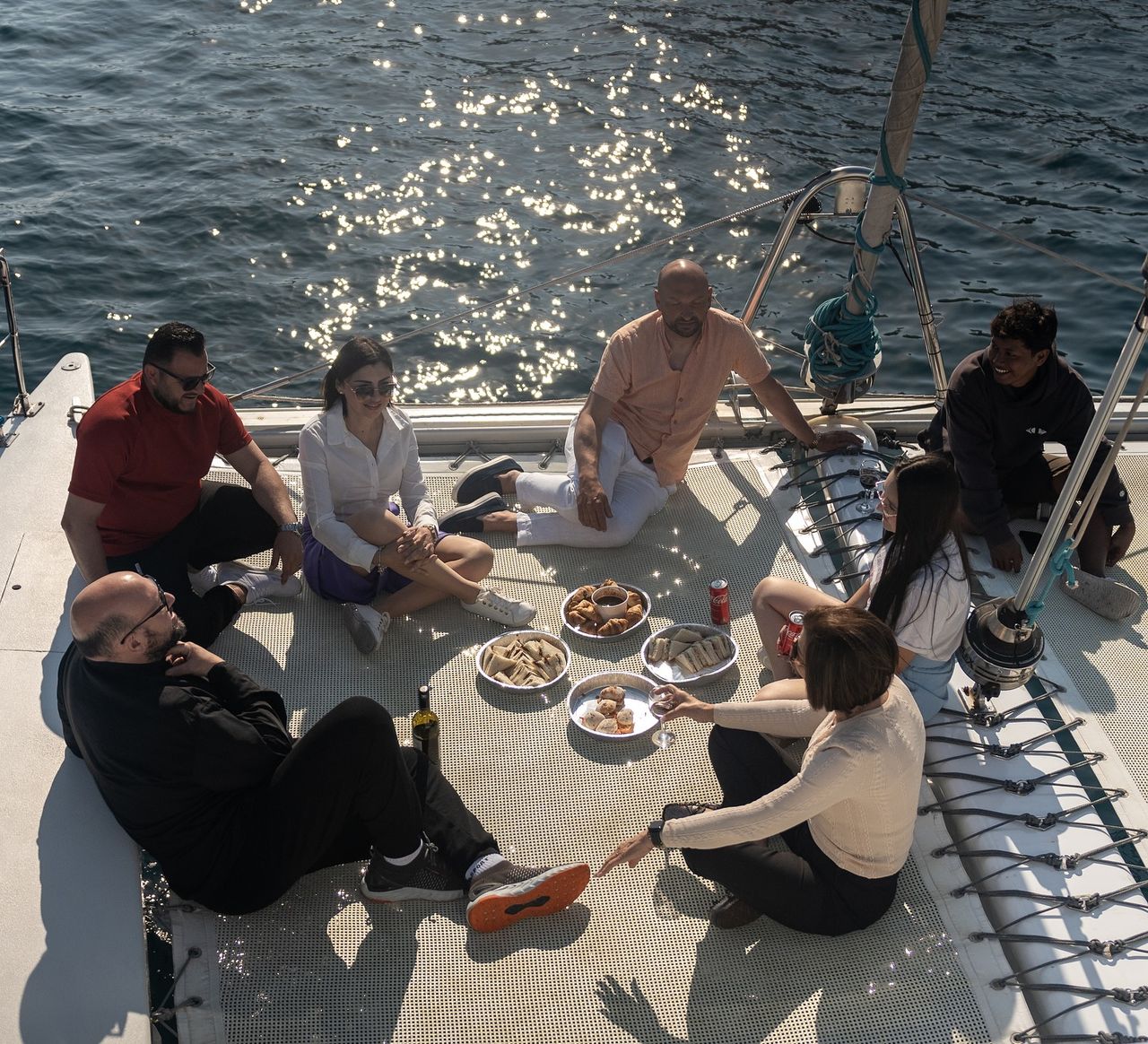 Guests dining and relaxing on the trampoline deck of a catamaran off Malta — La Zingara and Chardonnay sail private charters from Sliema.
