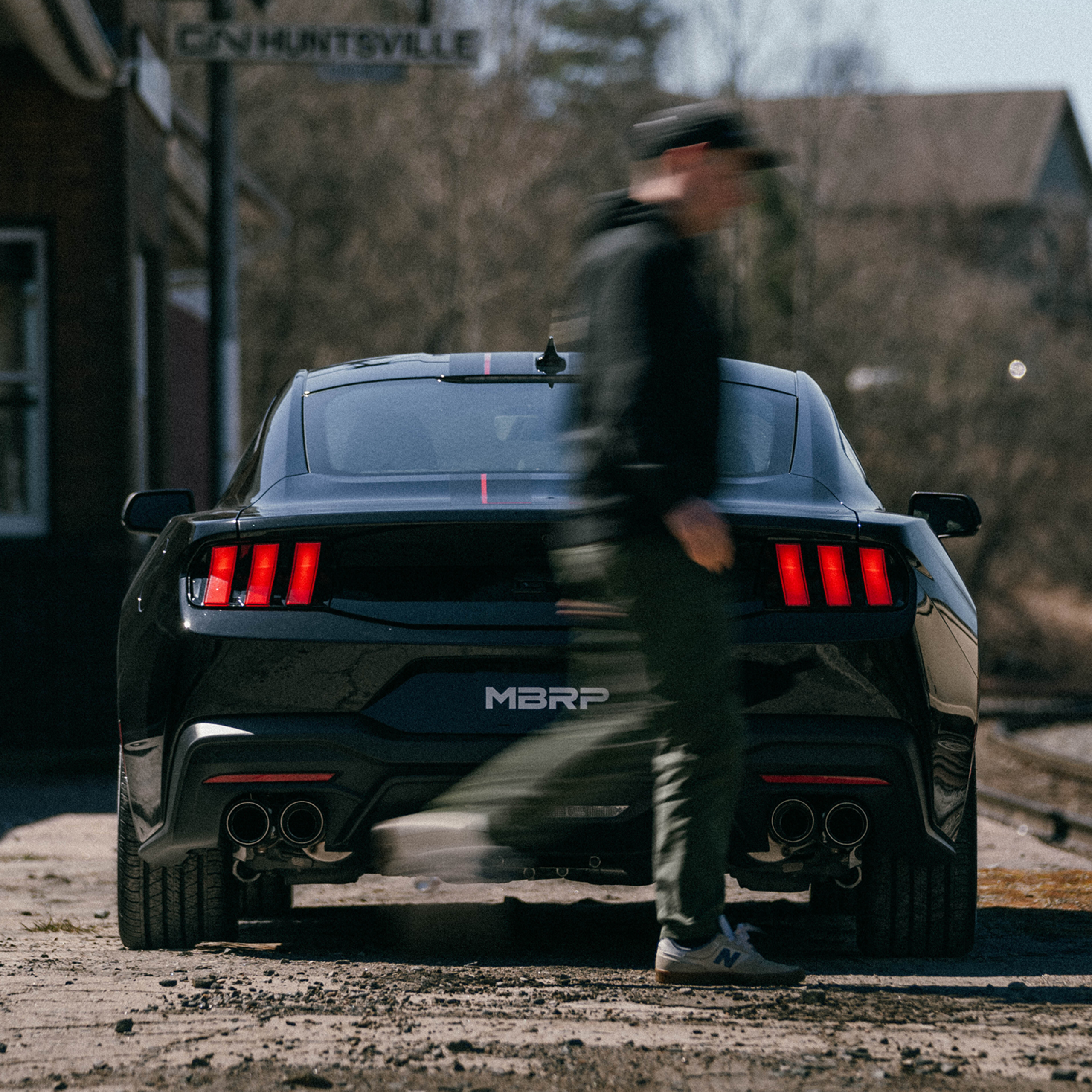 Black Mustang at railway with man walking past