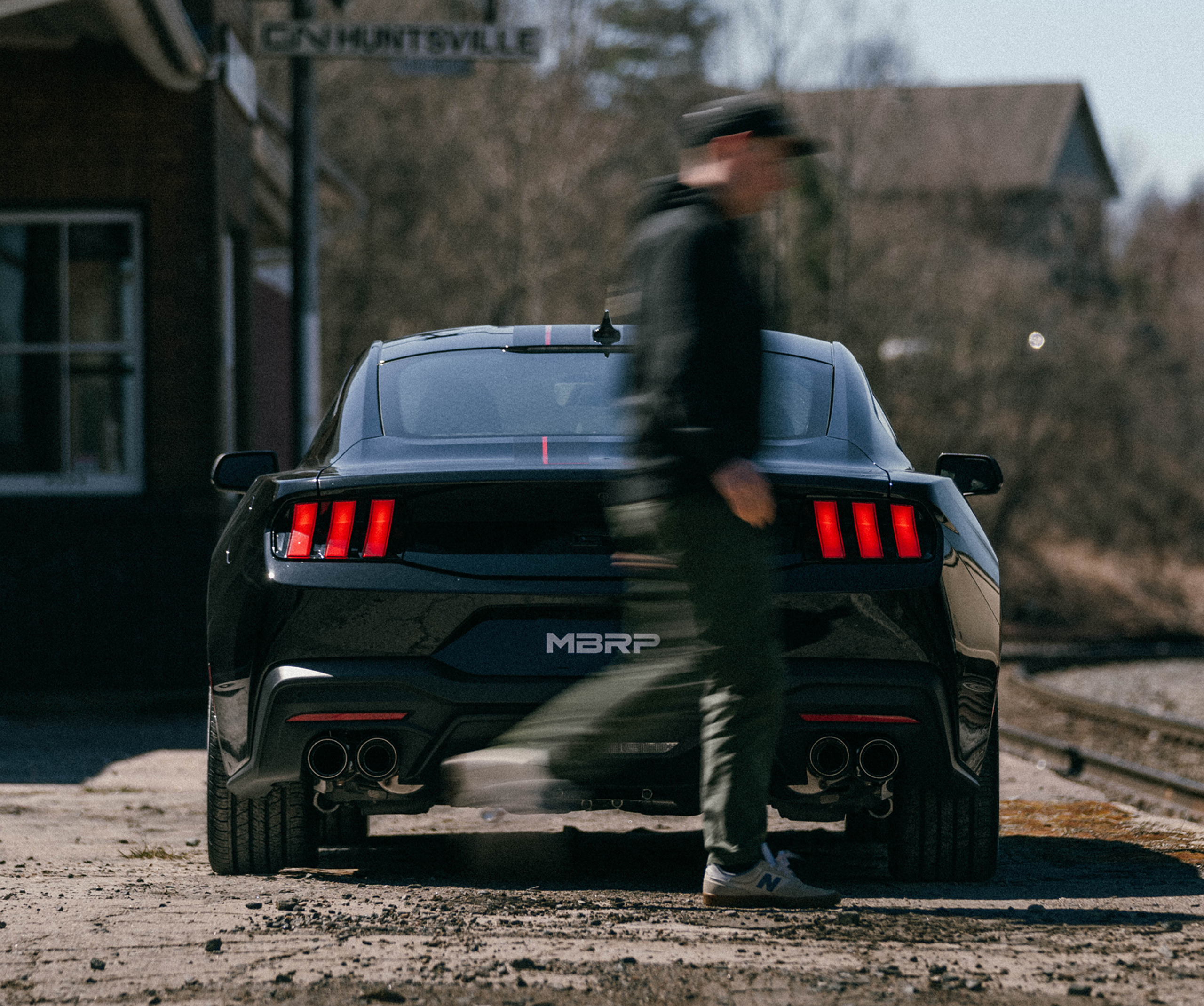 Black Mustang at railway with man walking past