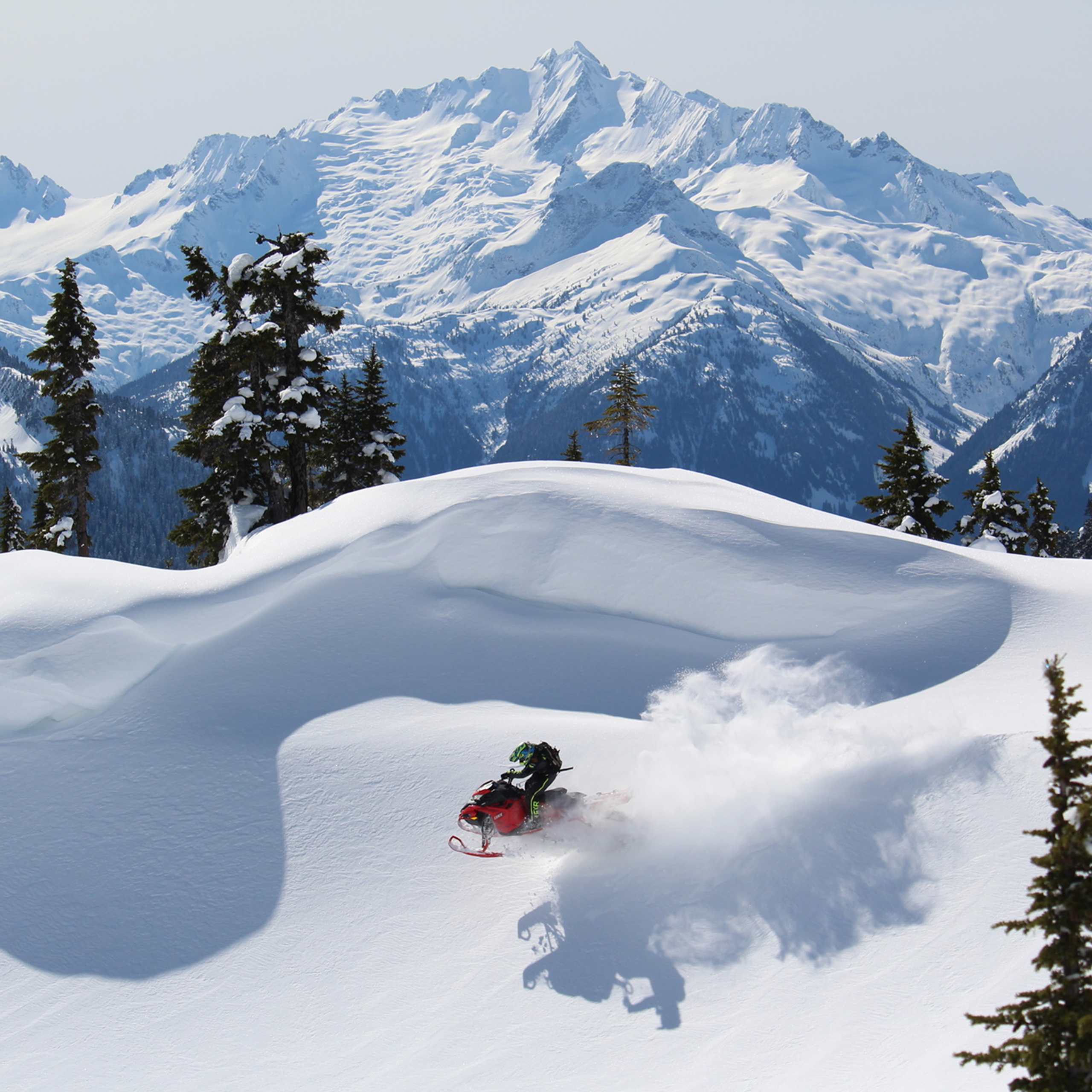 Snowmobile in the mountains catching a jump on a bluebird day