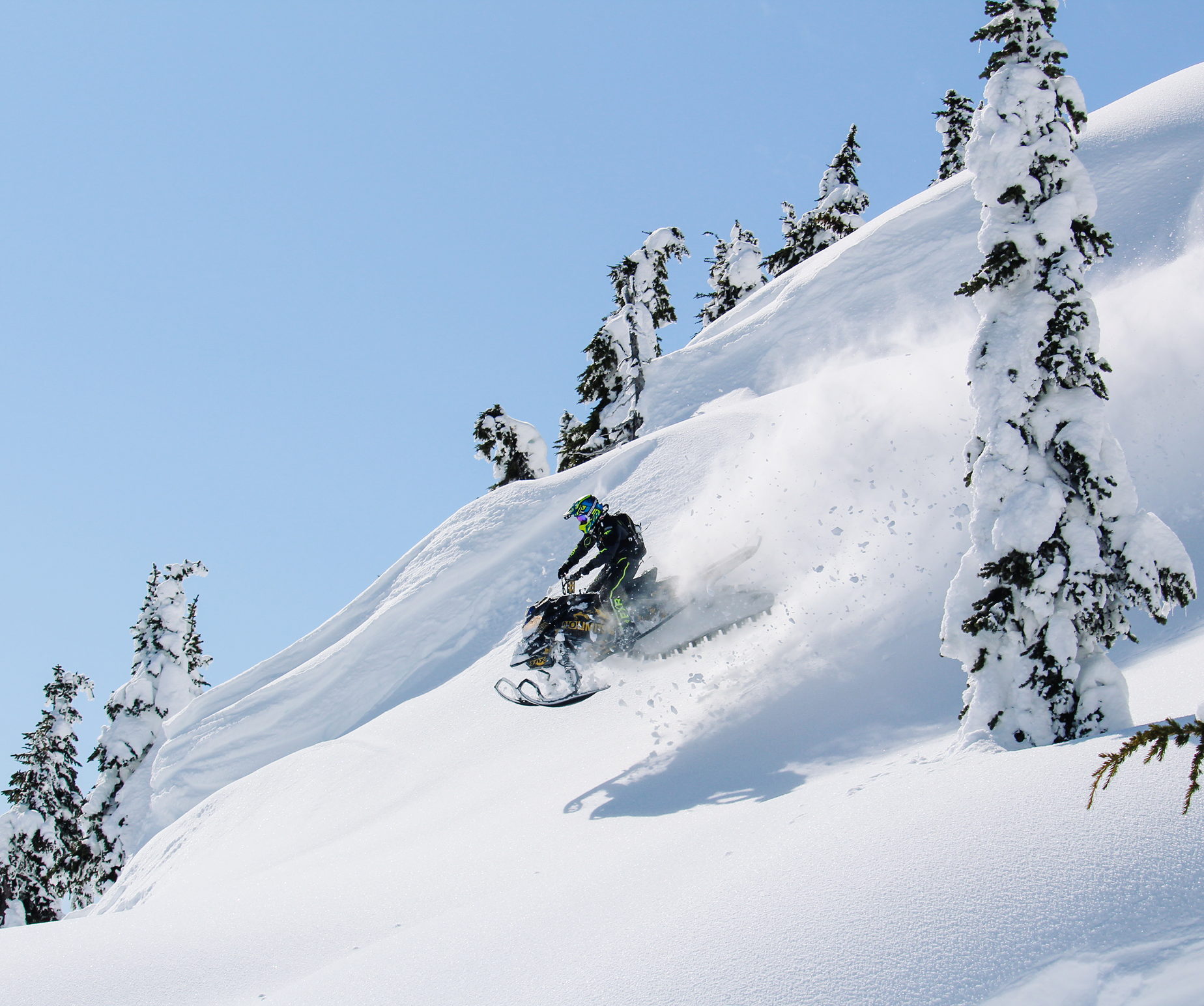 Snowmobile in the mountains catching a jump on a bluebird day