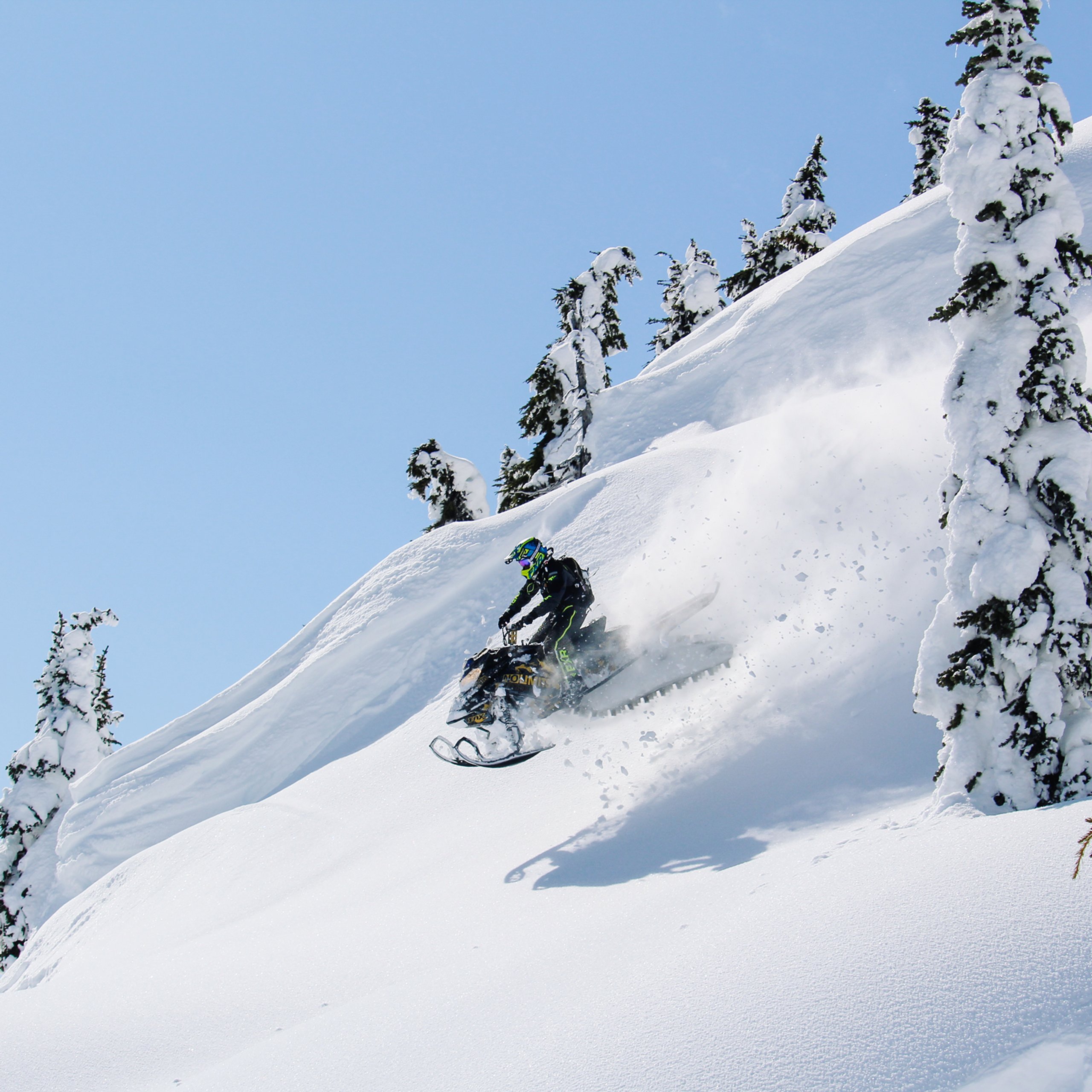 Snowmobile in the mountains catching a jump on a bluebird day