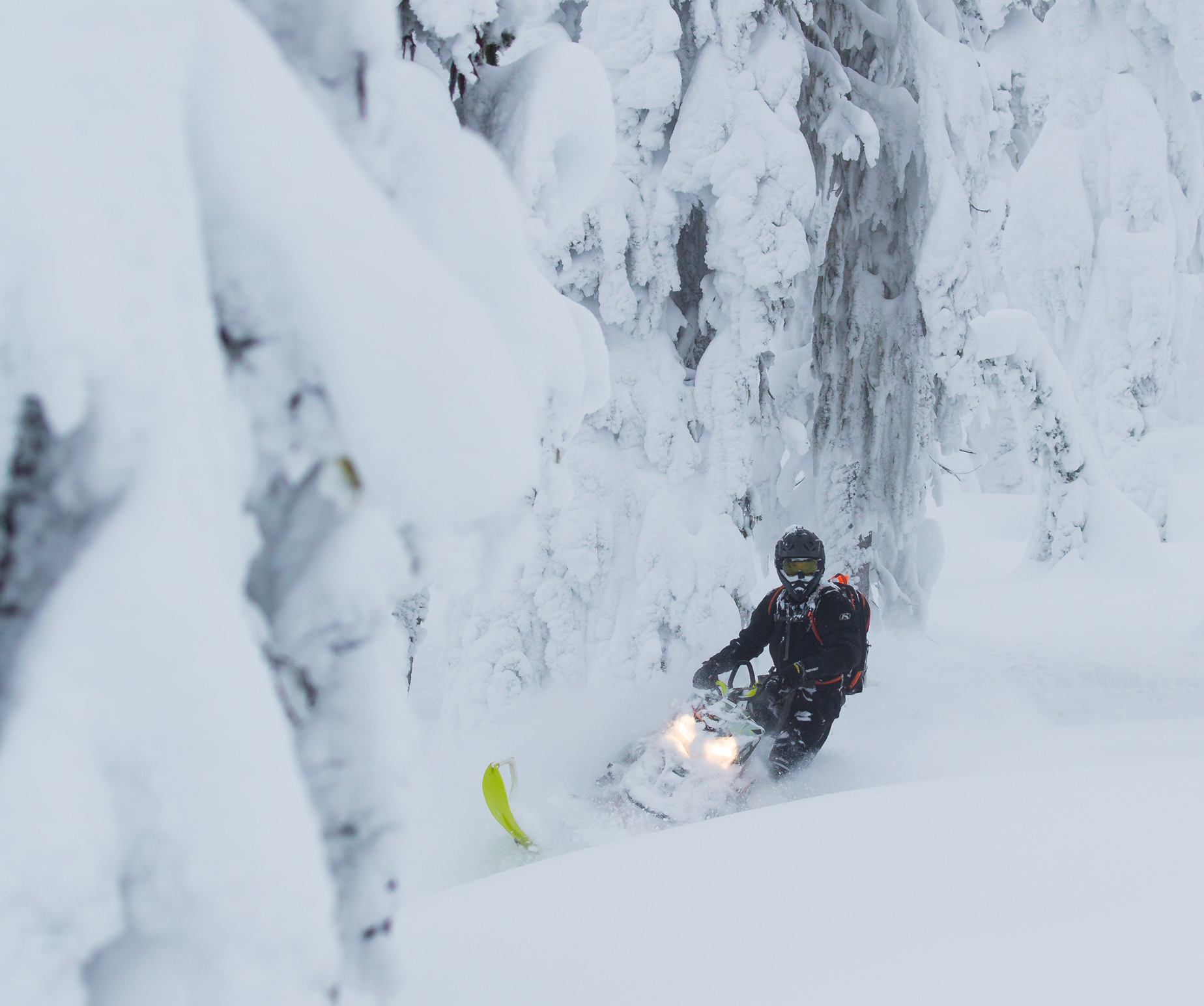 Snowmobile getting deep into the snow on a turn in the mountains with trees covered in snow