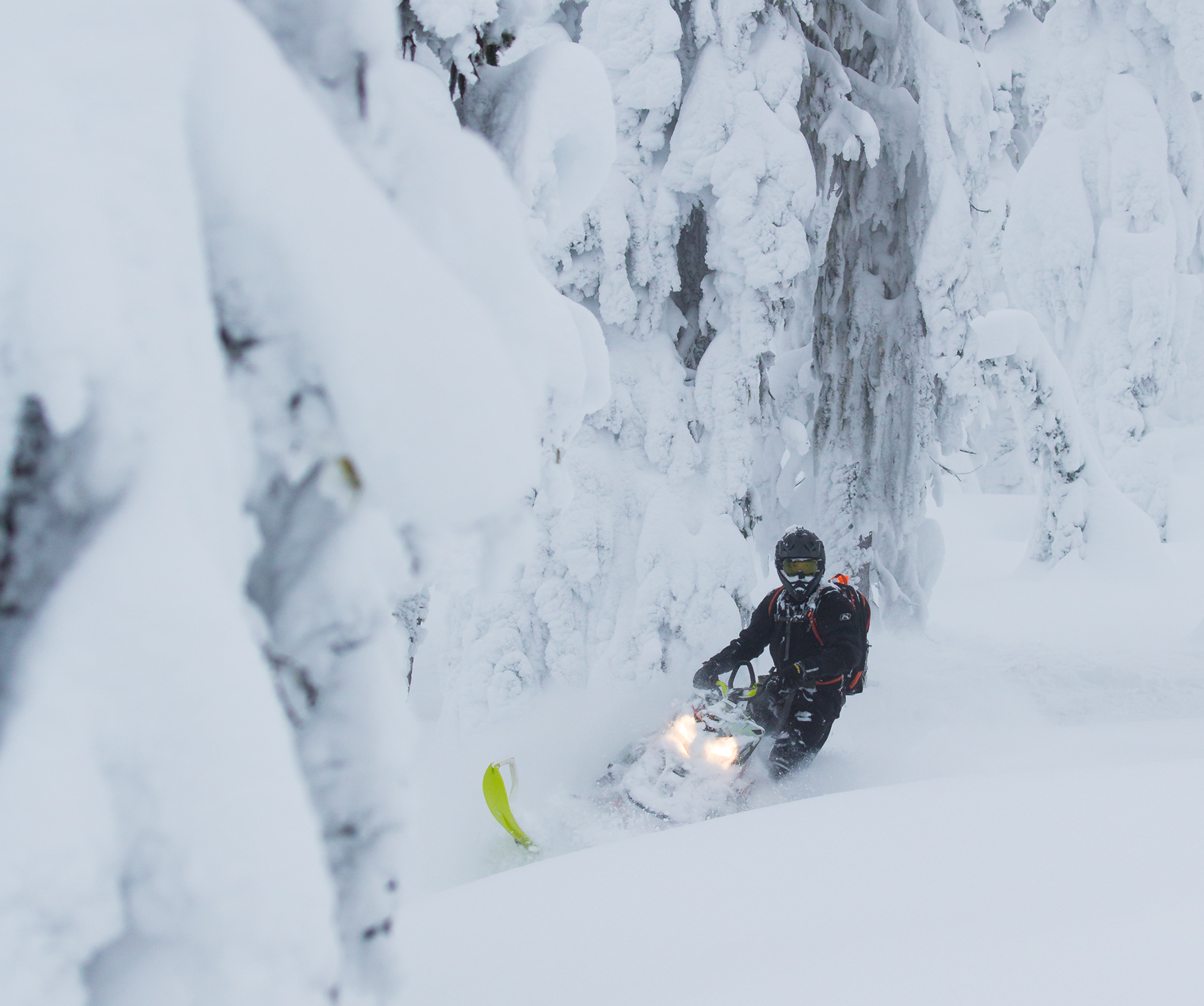 Snowmobile getting deep into the snow on a turn in the mountains with trees covered in snow