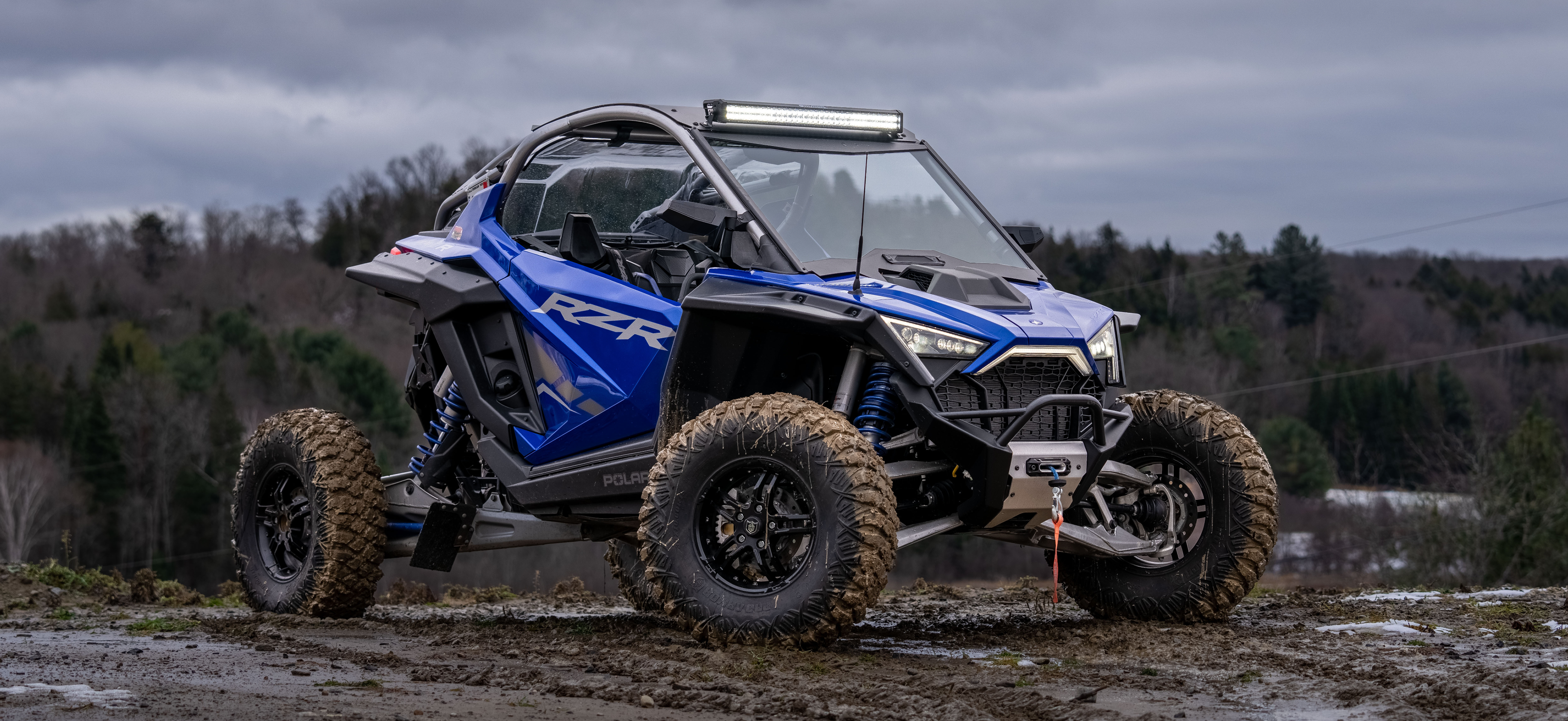 Polaris RZR in cobalt blue with an mbrp exhaust and lighting kit riding through the mud in late fall