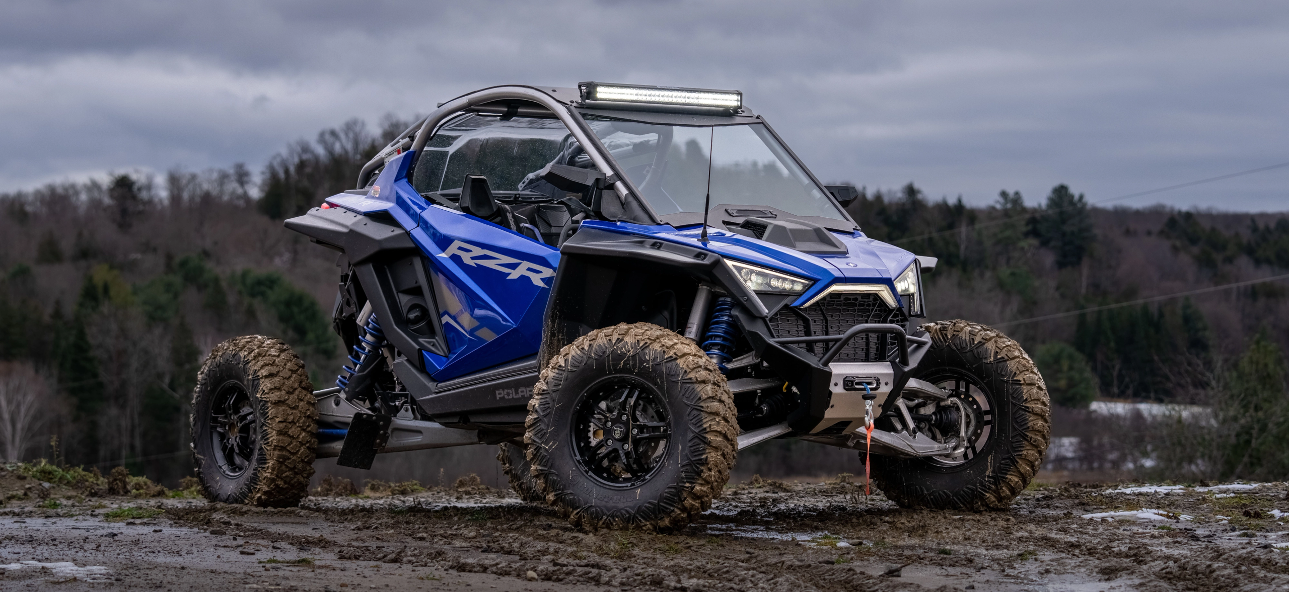 Polaris RZR in cobalt blue with an mbrp exhaust and lighting kit riding through the mud in late fall
