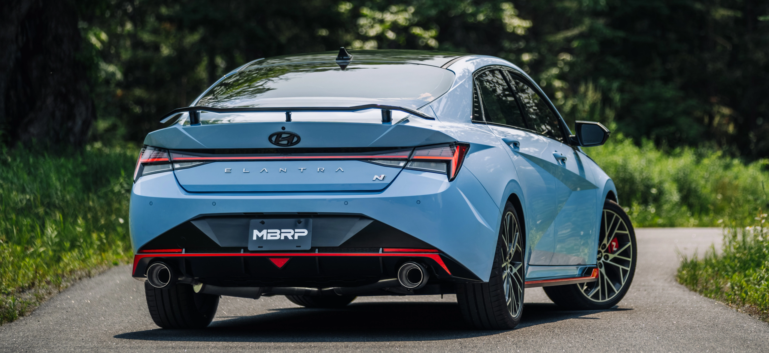 Light blue Hyundai Elantra with red trim showing an mbrp exhaust kit off on a sunny day in summer