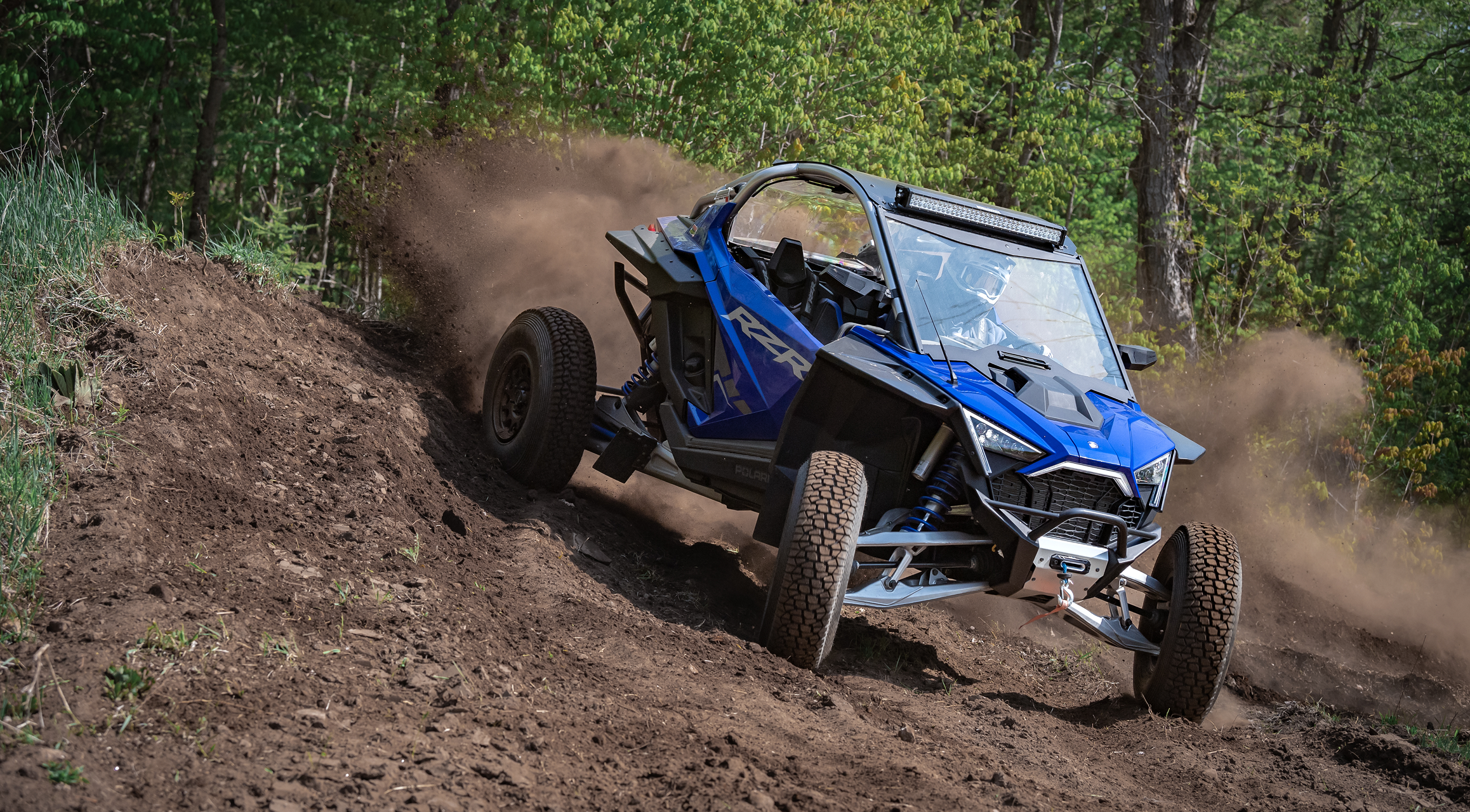 RXR SXS driving through the woods throwing up dirt after