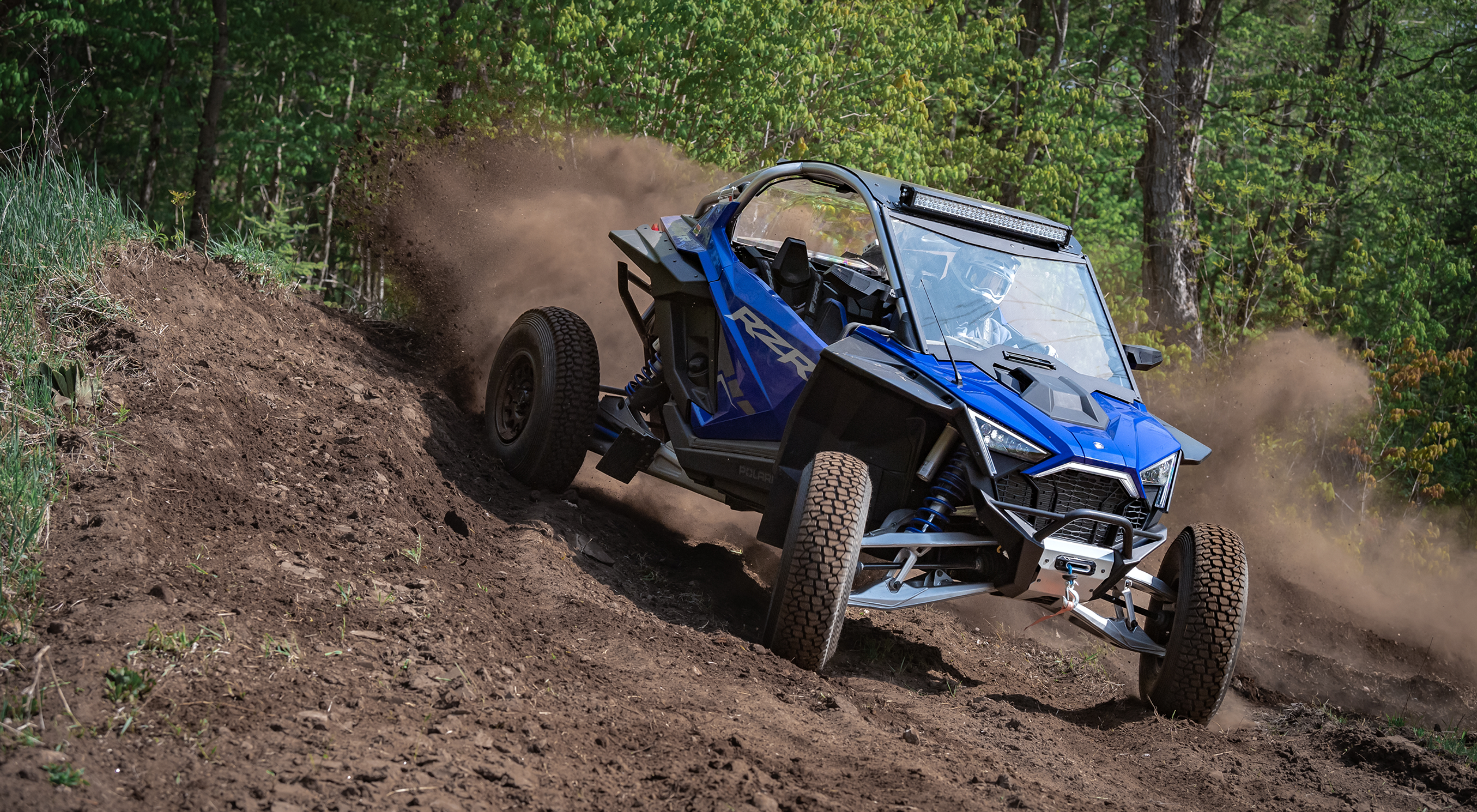 RXR SXS driving through the woods throwing up dirt after