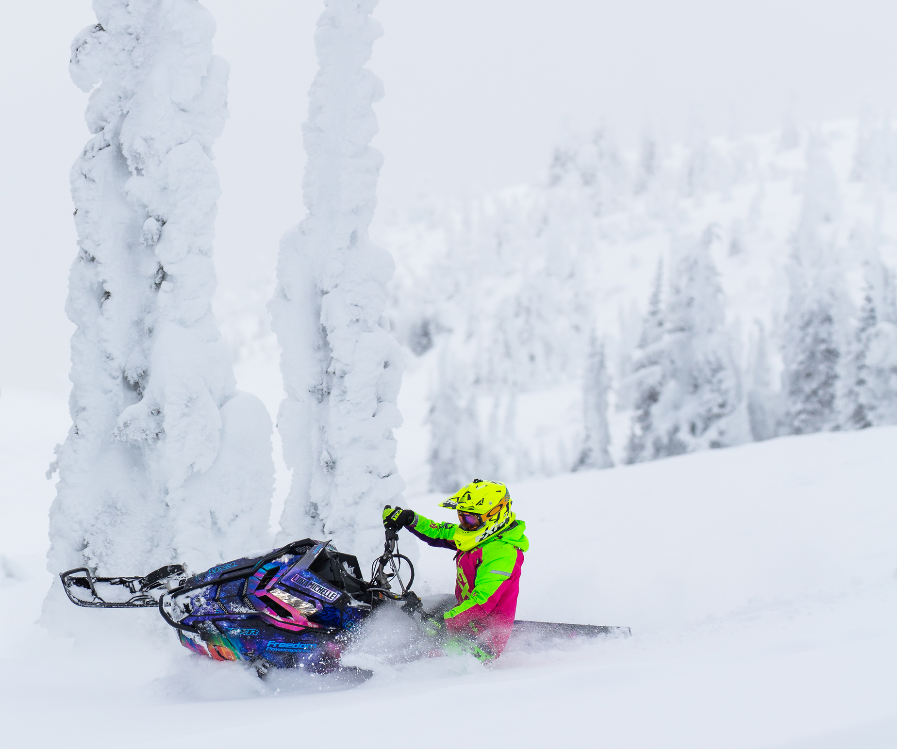 Snowmobile getting deep into the snow on a turn in the mountains with trees covered in snow