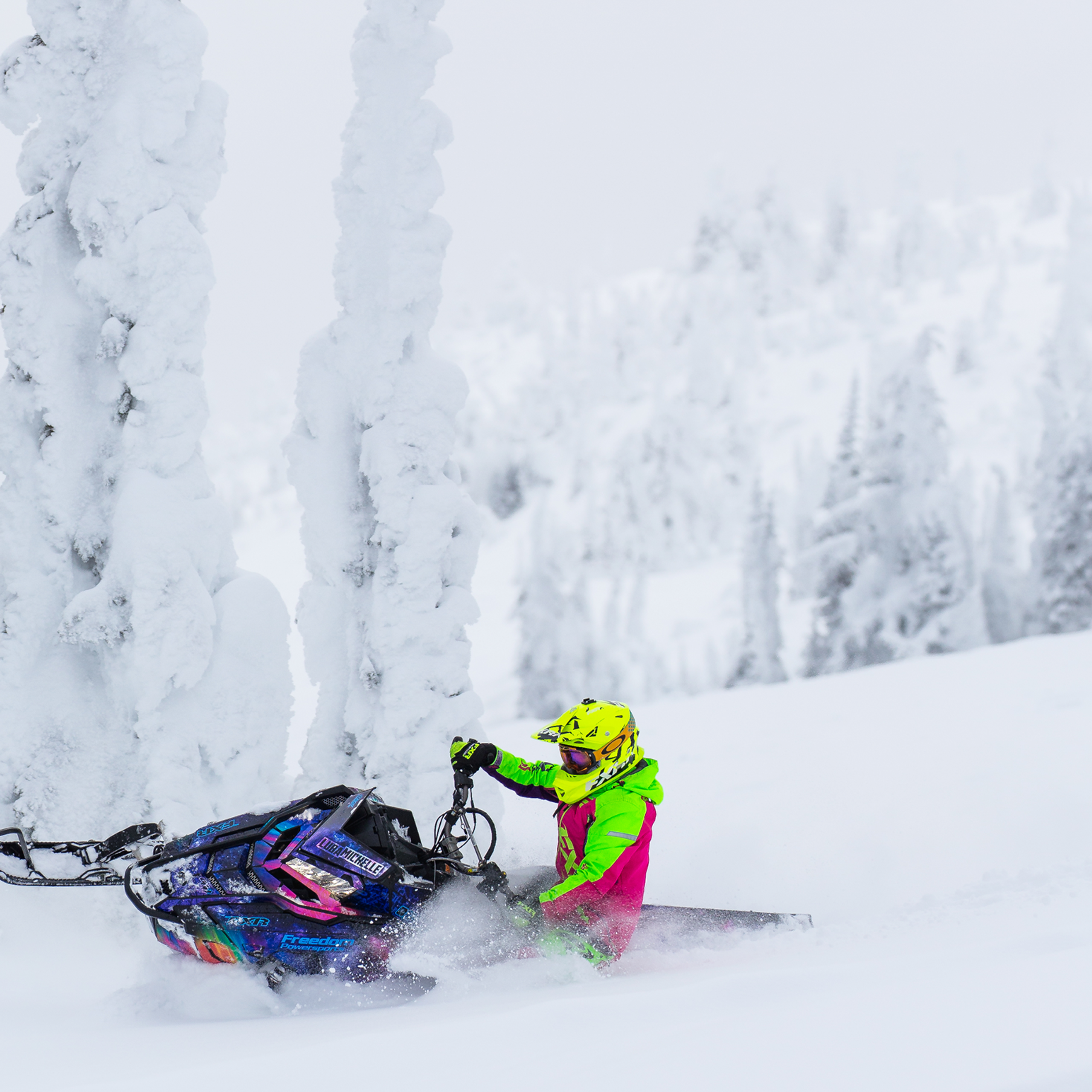 Snowmobile getting deep into the snow on a turn in the mountains with trees covered in snow