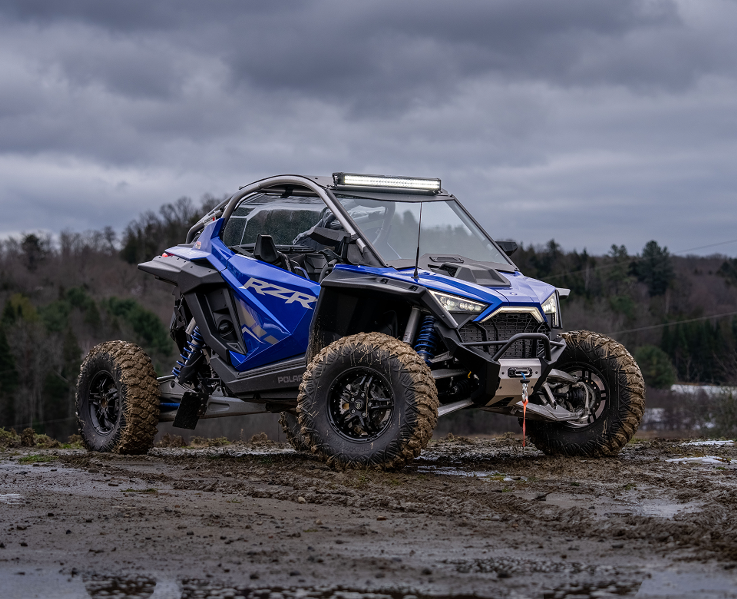 Polaris RZR in cobalt blue with an mbrp exhaust and lighting kit riding through the mud in late fall