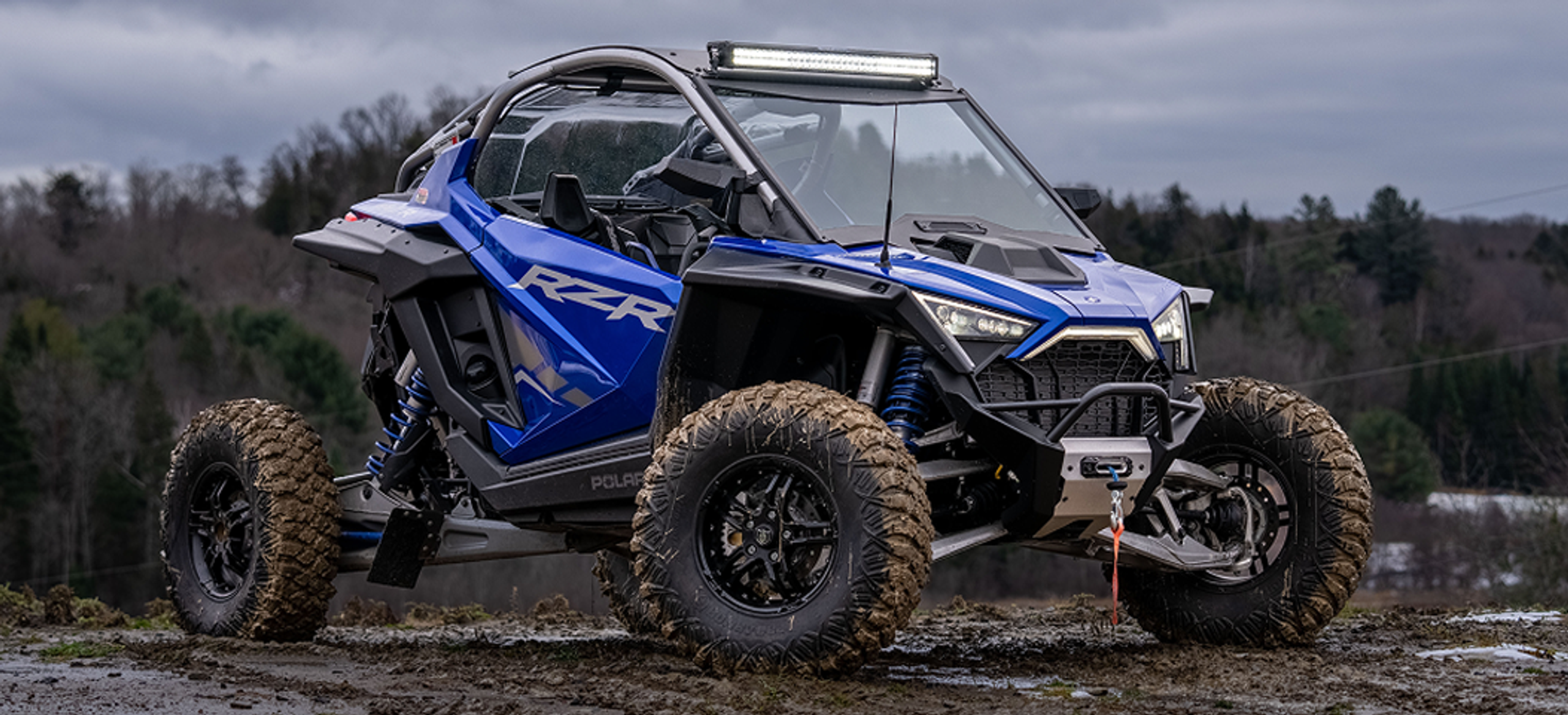 Polaris RZR in cobalt blue with an mbrp exhaust and lighting kit riding through the mud in late fall