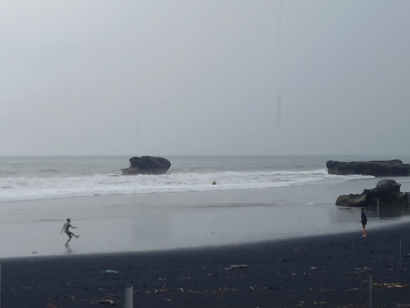 A photograph of two boys or young men on a beach in overcast, misty weather, playing ball