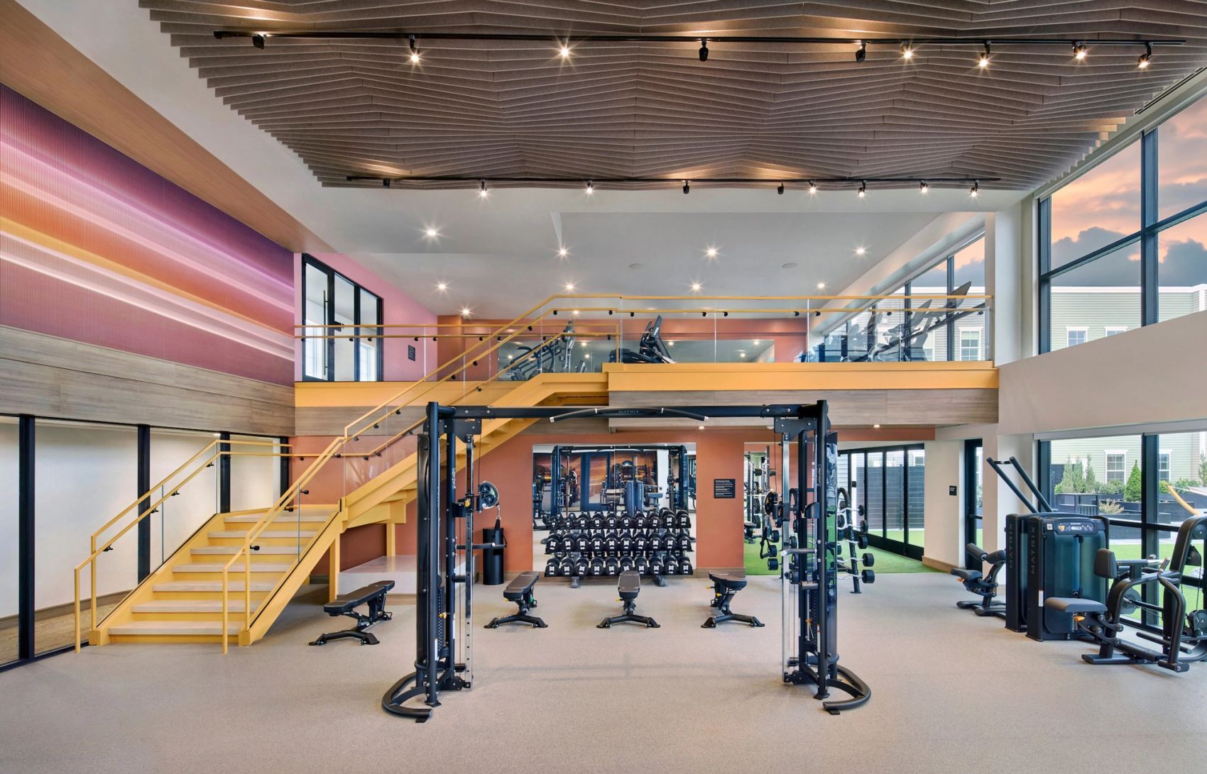 Large, multi-level fitness center with strength-training machines, cable equipment, free weights, benches, cardio equipment, and expansive windows.