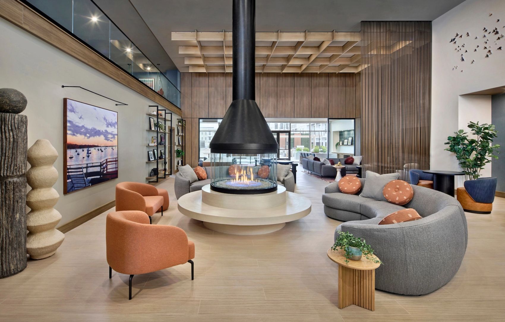 Welcoming resident lounge with a central fireplace, curved sofas, contemporary lounge chairs, and warm wood architectural details.