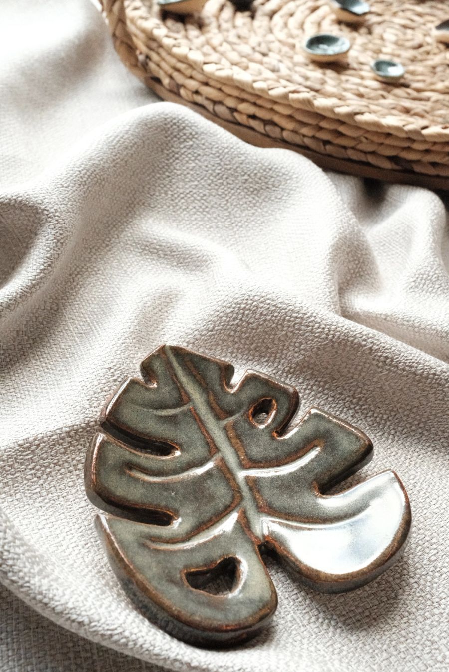 A sage-green ceramic dish carved in the shape of a monstera leaf, resting on white linen