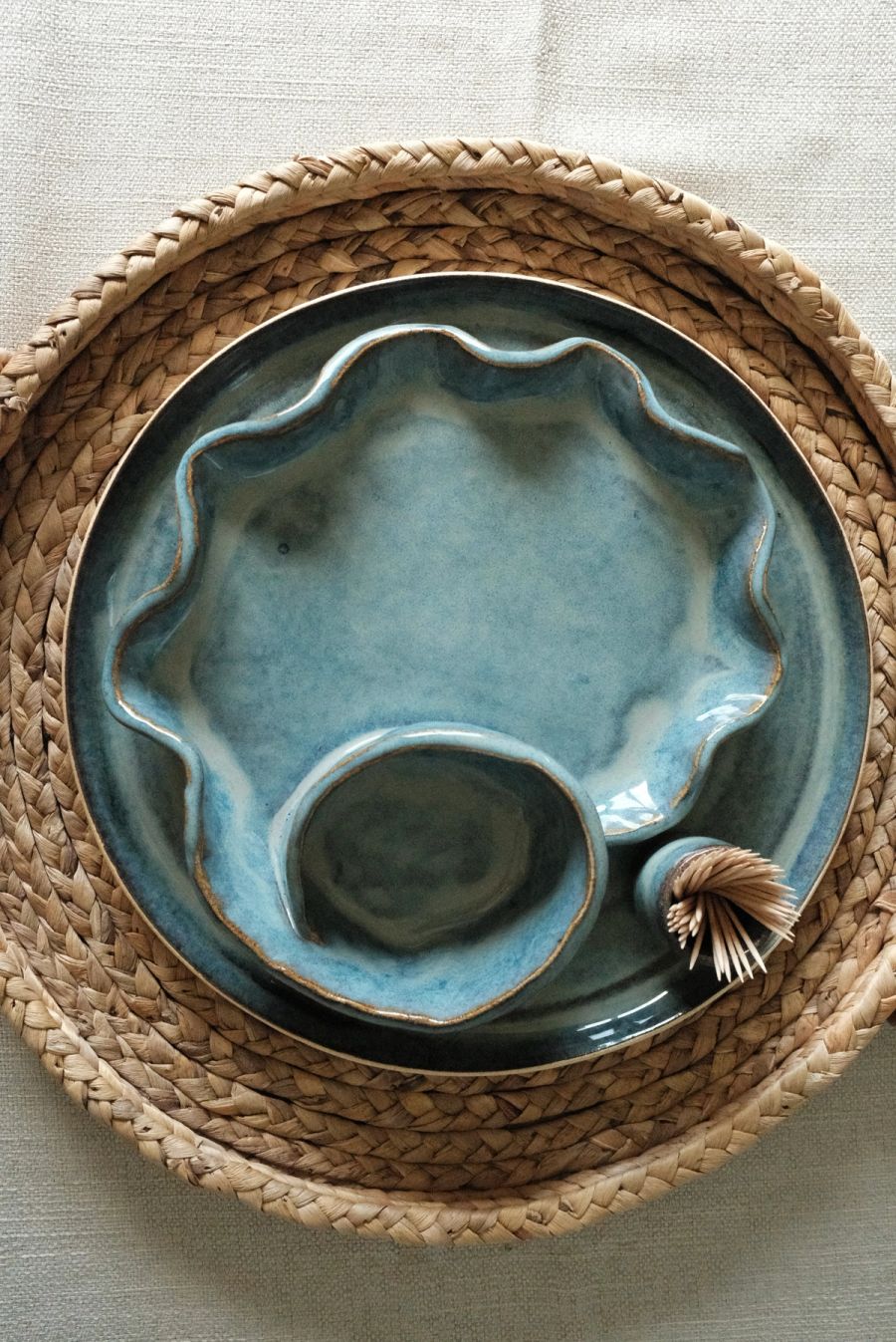 A blue ruffle-edged plate nested with a small blue dip bowl on a round woven tray