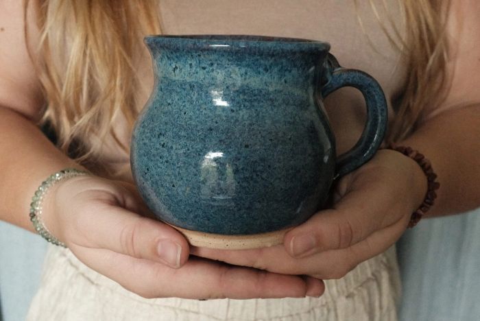 Kelly cradling a speckled blue-glazed mug in both hands