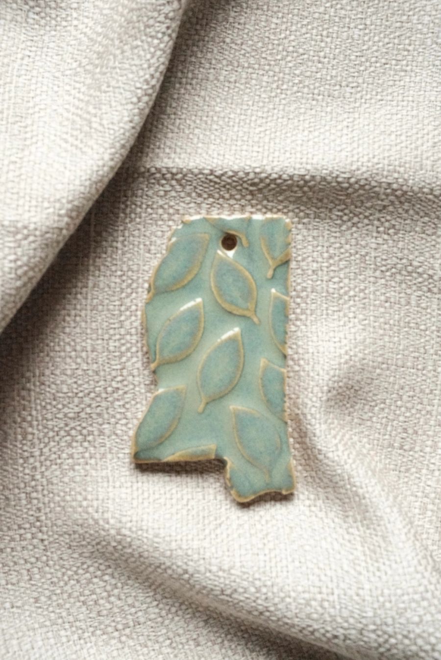 A pale celadon dish shaped like the state of Mississippi, pressed with a leaf-and-vine pattern, on linen
